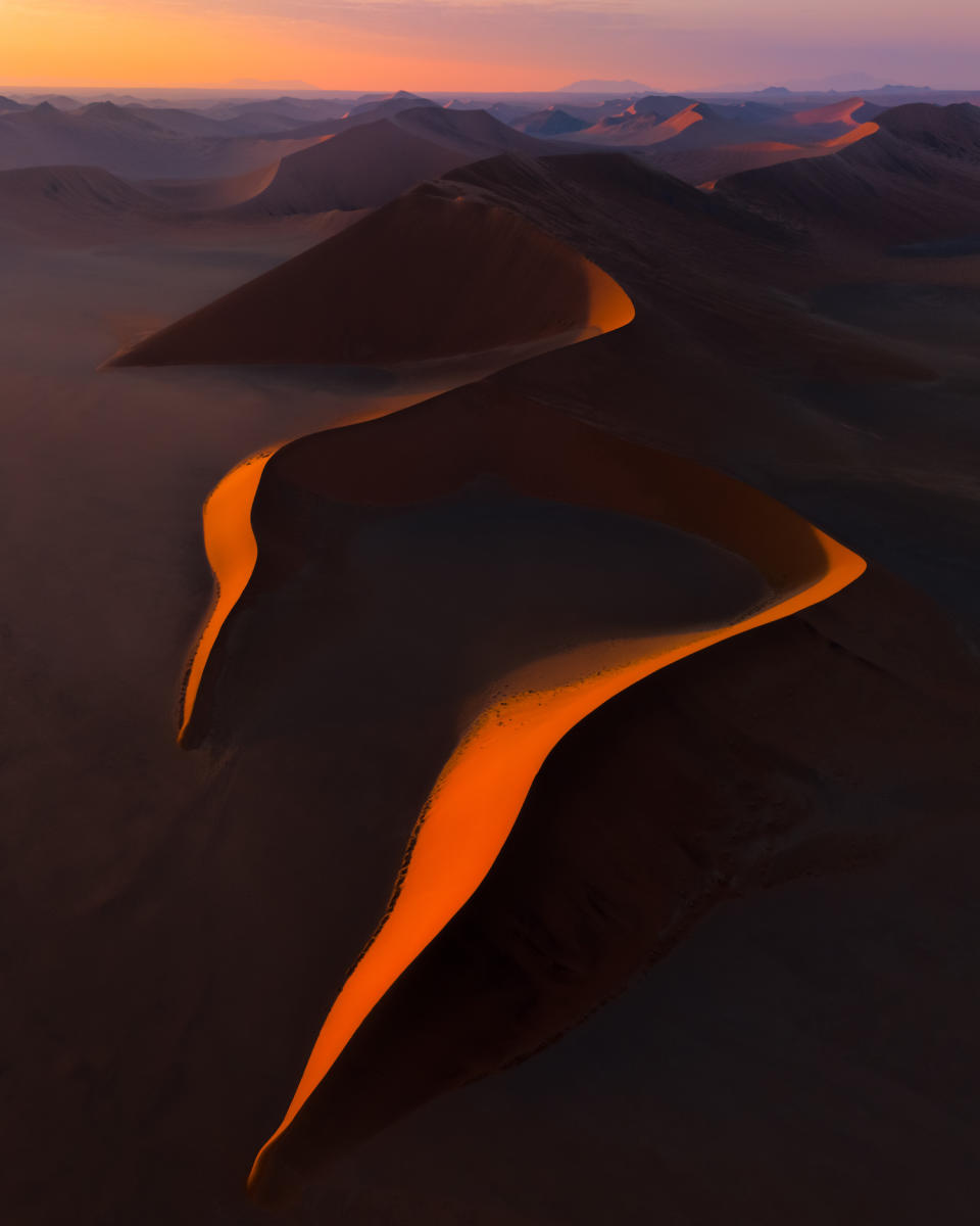 Sand dunes stretch across a desert at sunset