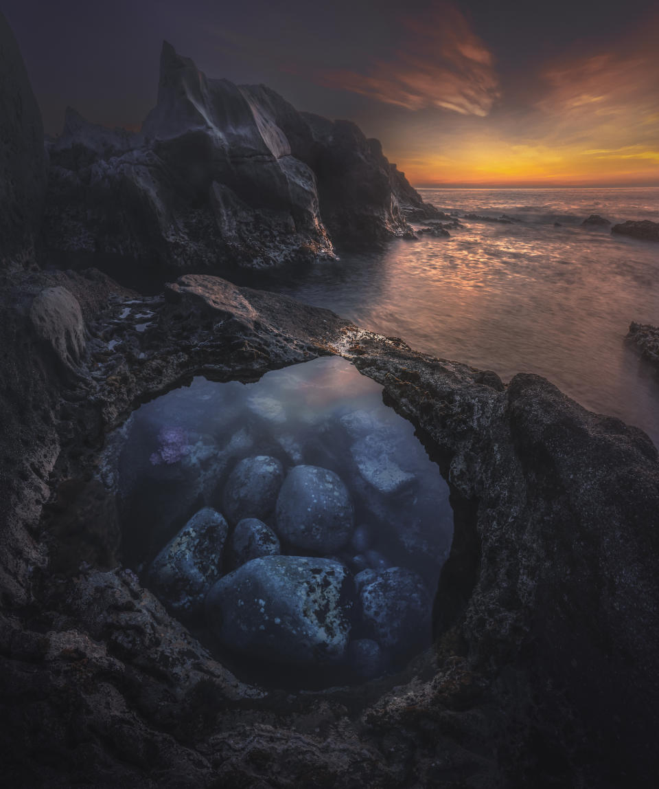 Stones in a small pool of water in the foreground. Sunset in the background next to impressive peaks