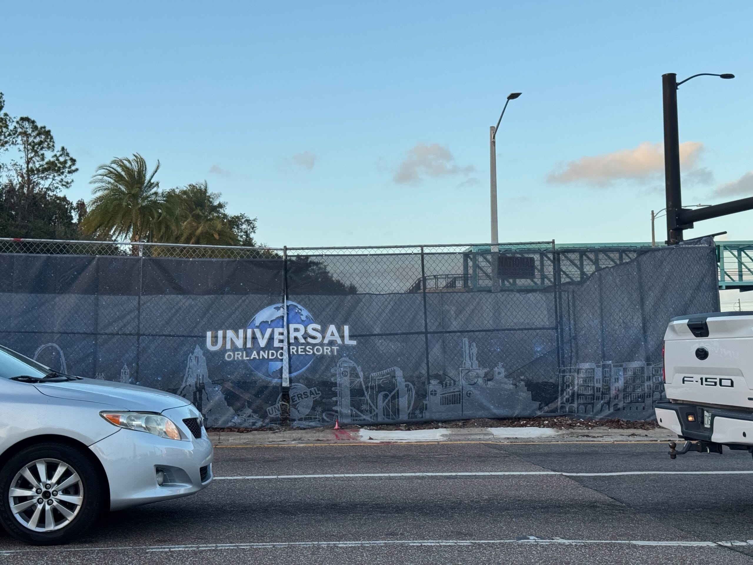 Cars drive past a construction site with a Universal Orlando Resort banner on a fence.