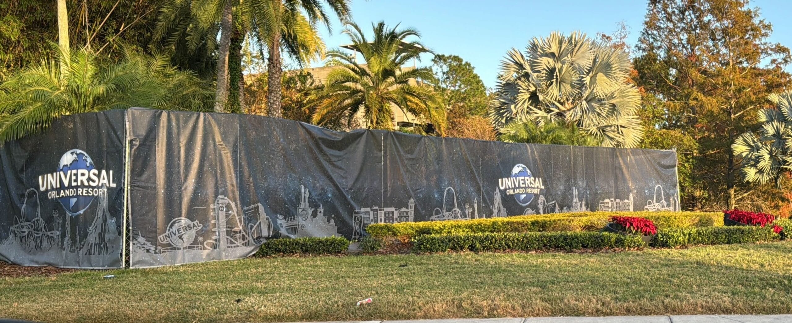 A banner with "Universal Orlando Resort" Theme park logos and illustrations cover a fence surrounded by palm trees and bushes.