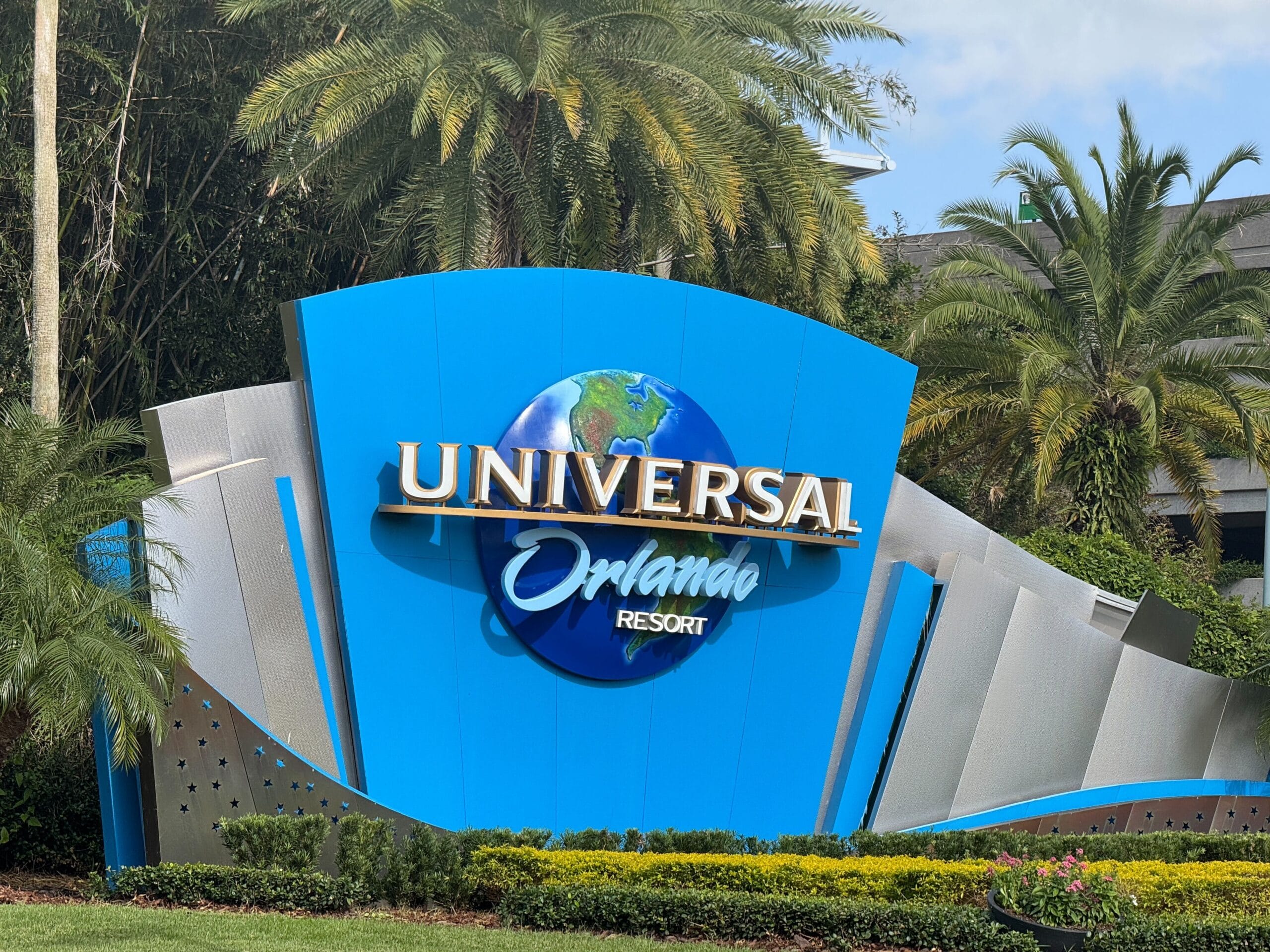 Universal Orlando Resort entrance sign with globe logo surrounded by palm trees and greenery.