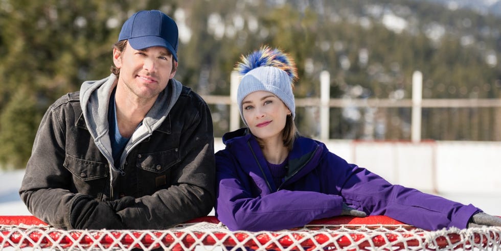 A man and a woman sit on a fence with a mountain in the background