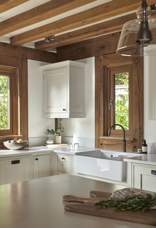 A small white kitchen with oak beams and oak window frames.