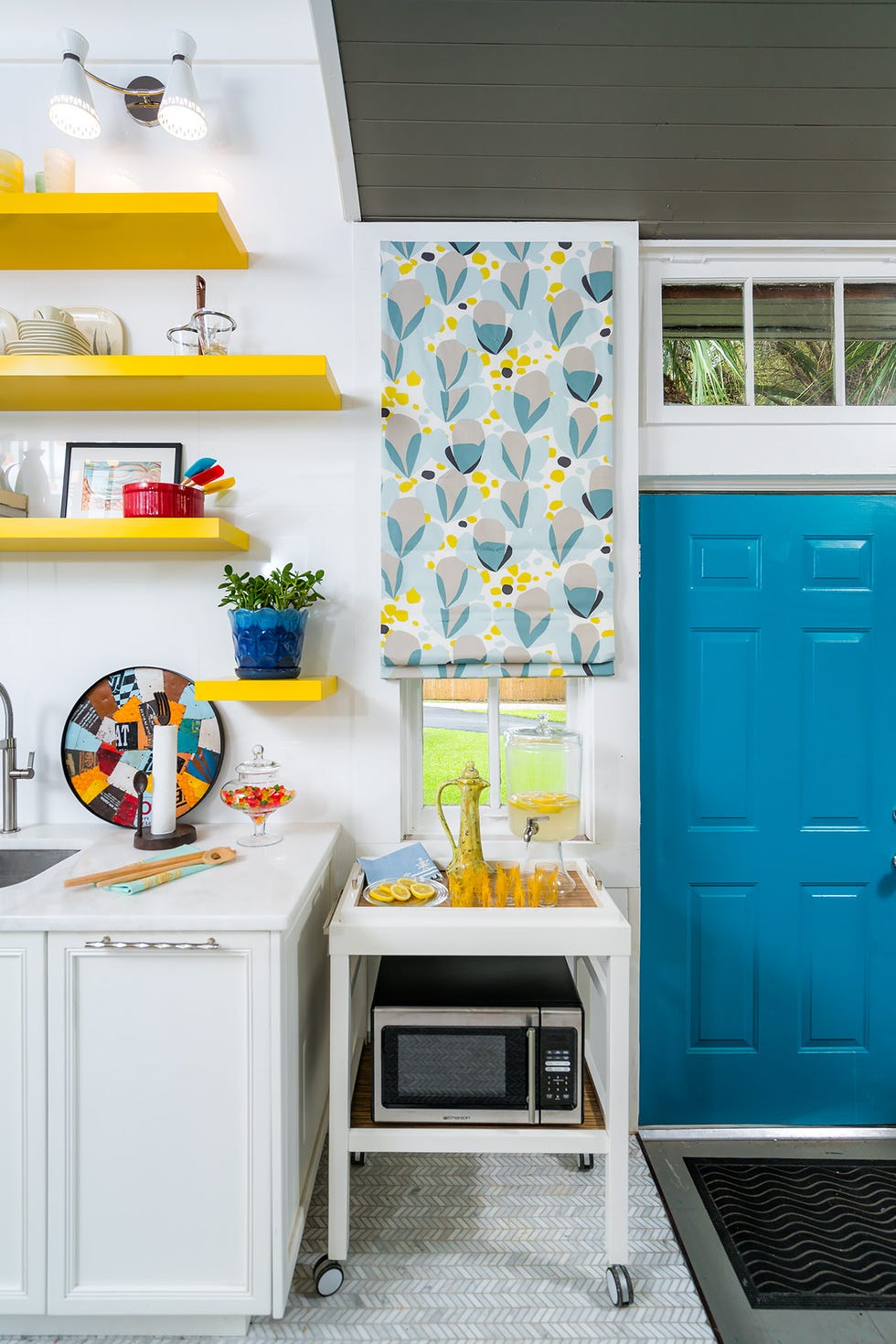 Bright kitchen area with a serving cart with colorful drink shelves and a blue door