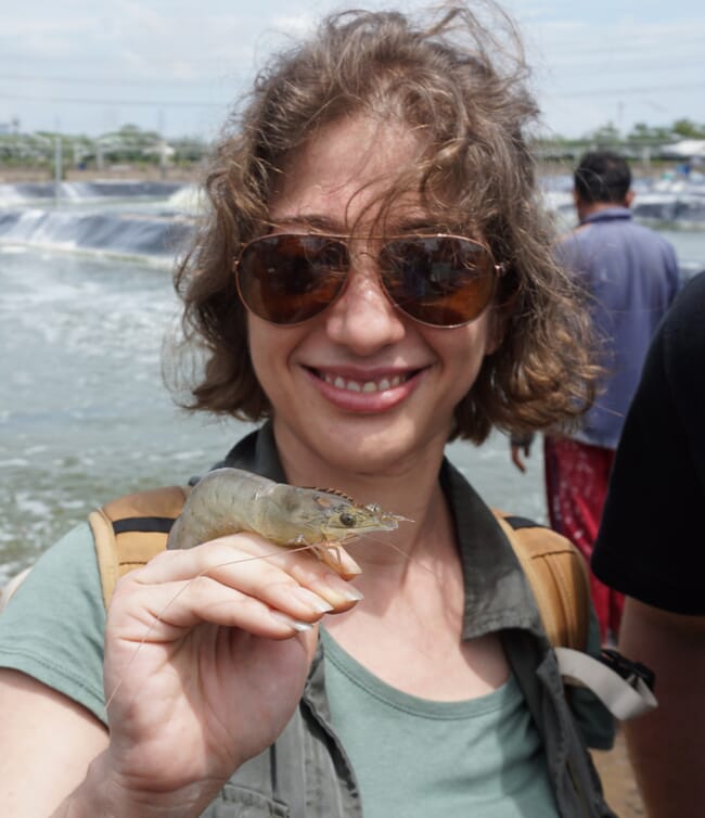 A woman holds a shrimp in her hand.