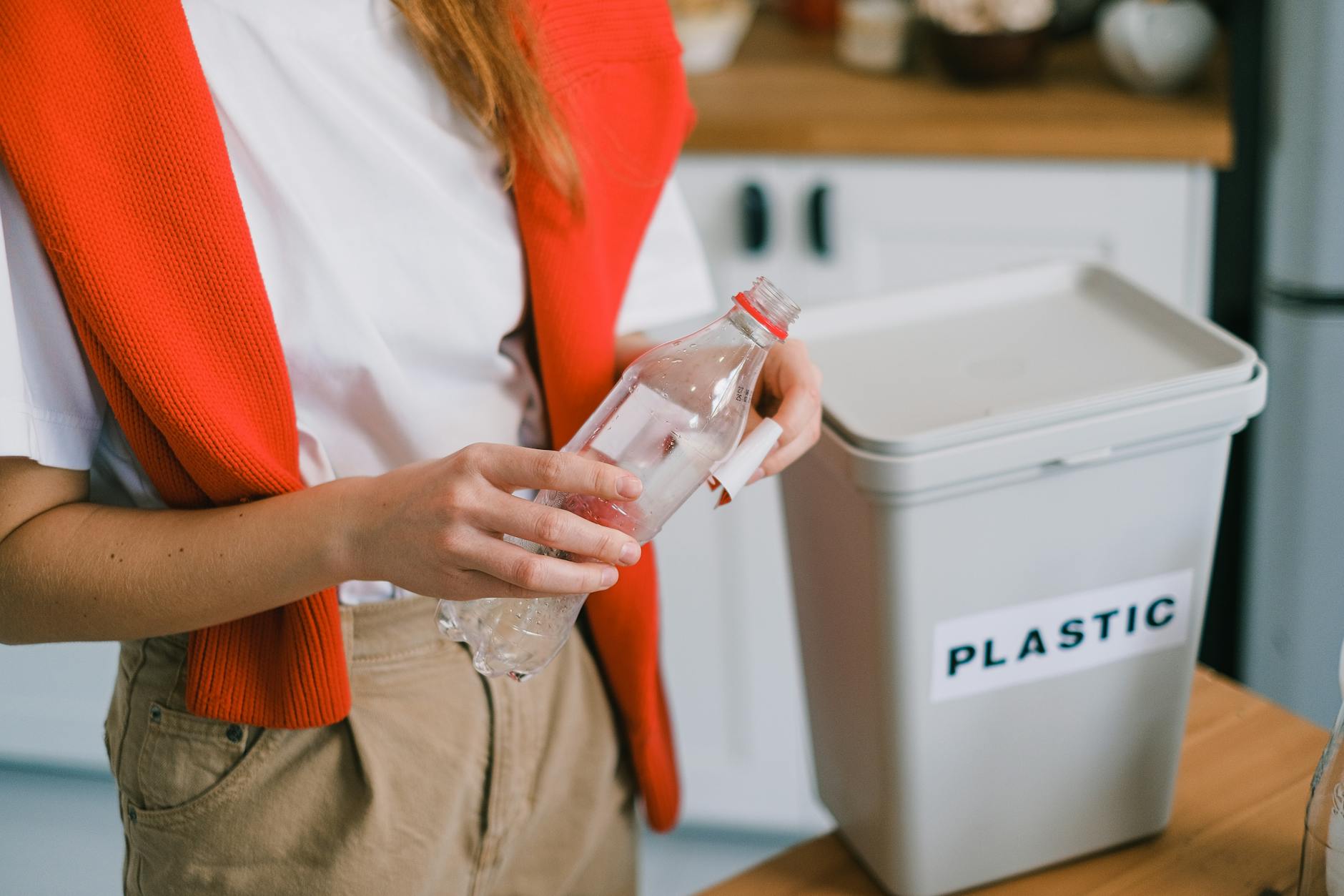 Person who holds a plastic bottle near a bucket