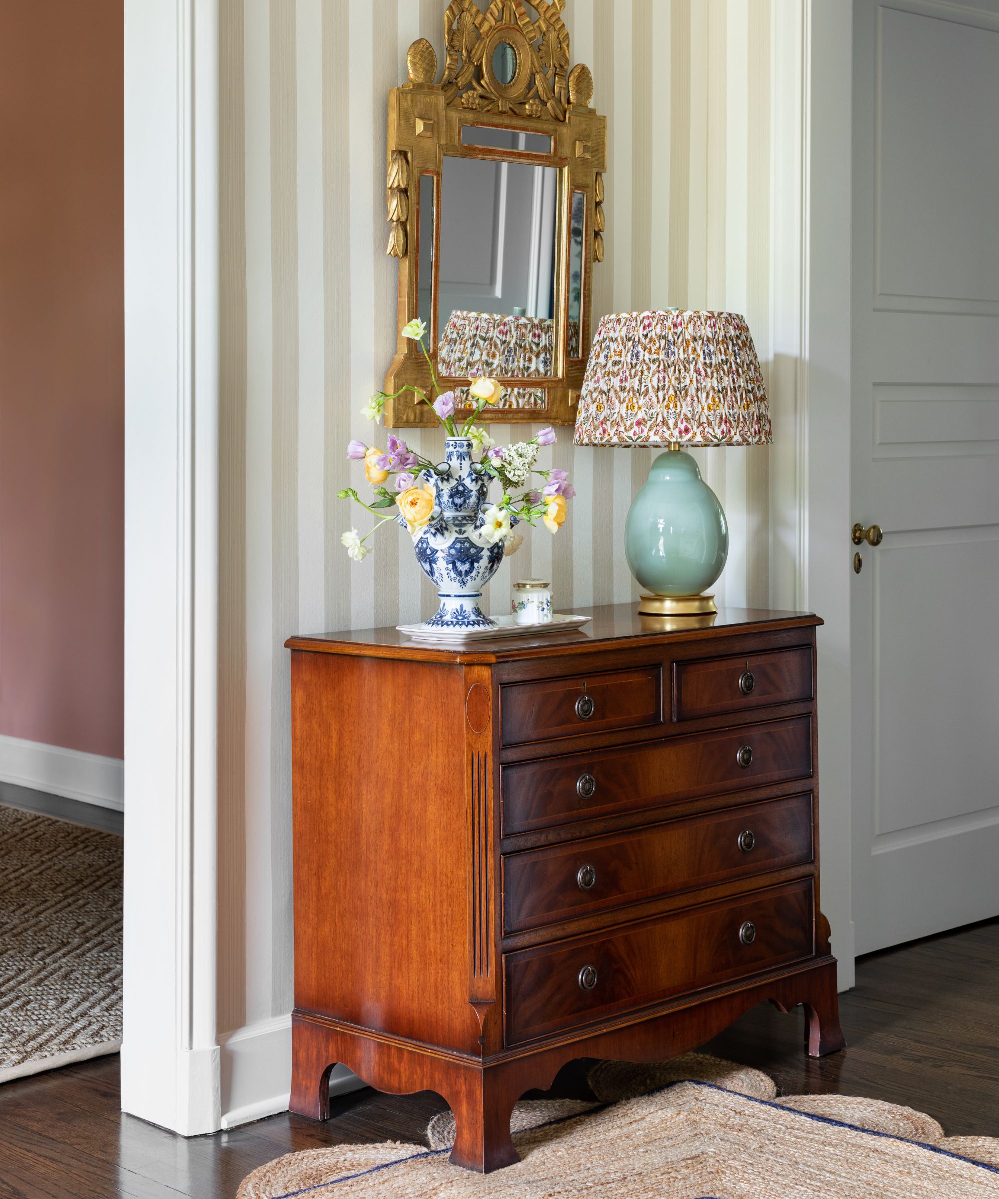 Hall with striped wallpaper and a oversbaked Jute carpet with an ancient mahogany sideboard with a blue table lamp and a flower vase