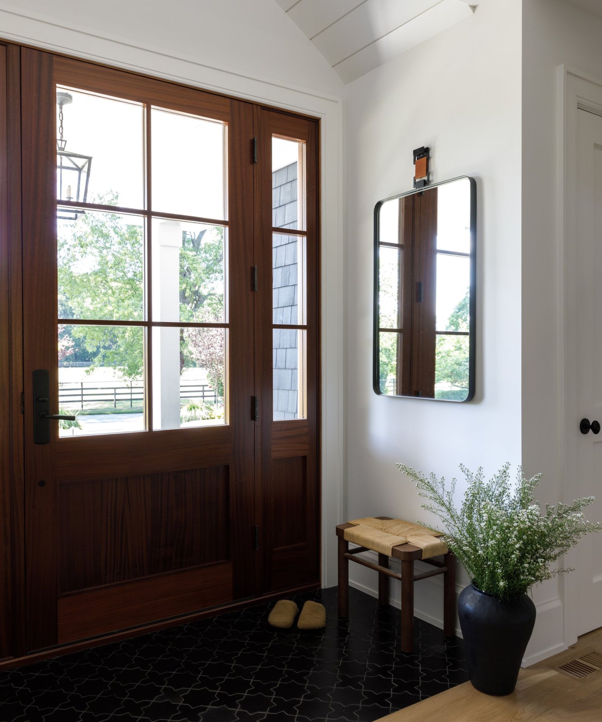 White small entrance with large mahogany doors with glass panels with a mirror and a small woven chair