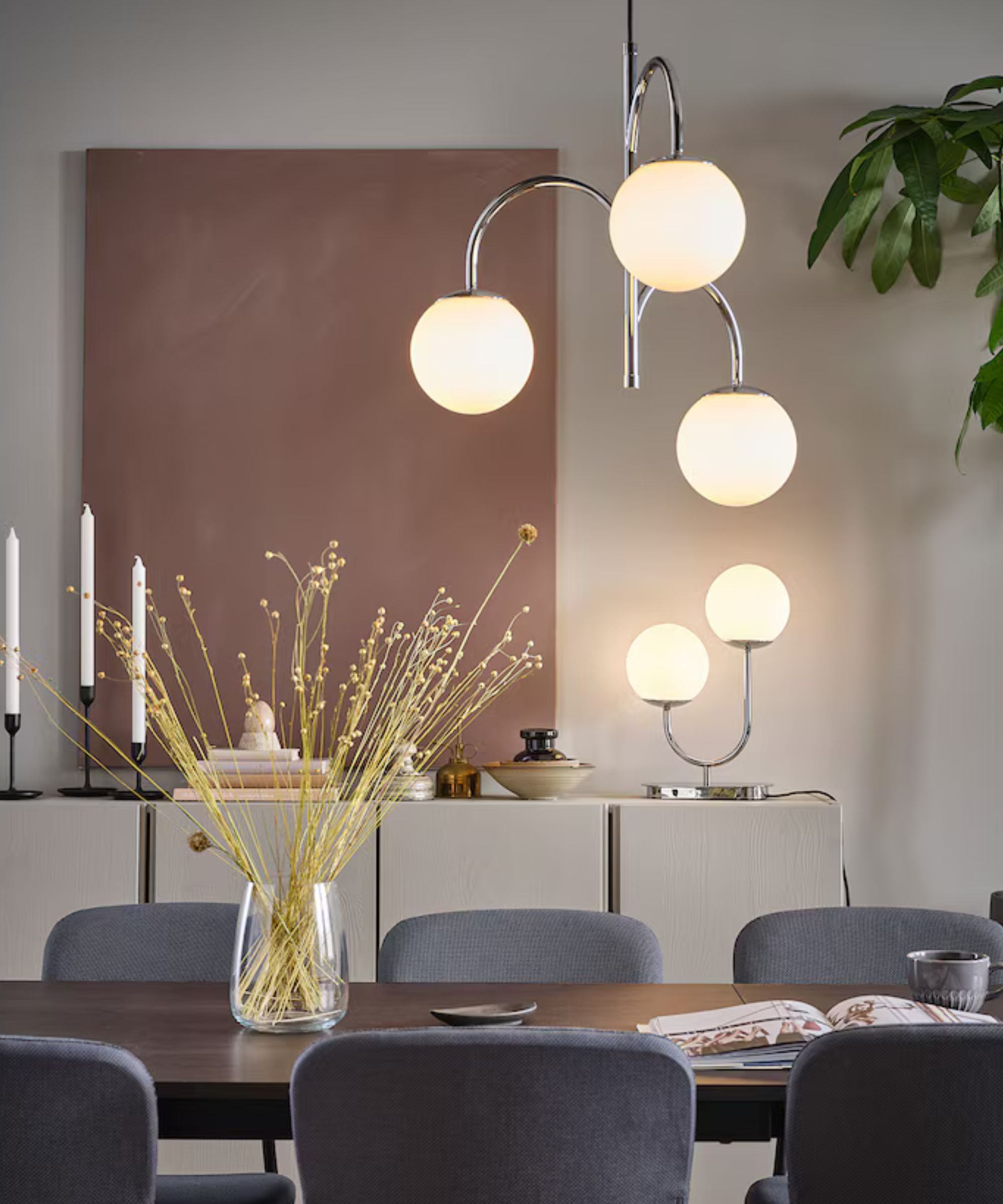 Ikea dining room with chrome globe lighting and pink works of art with gray chairs and wooden dining table