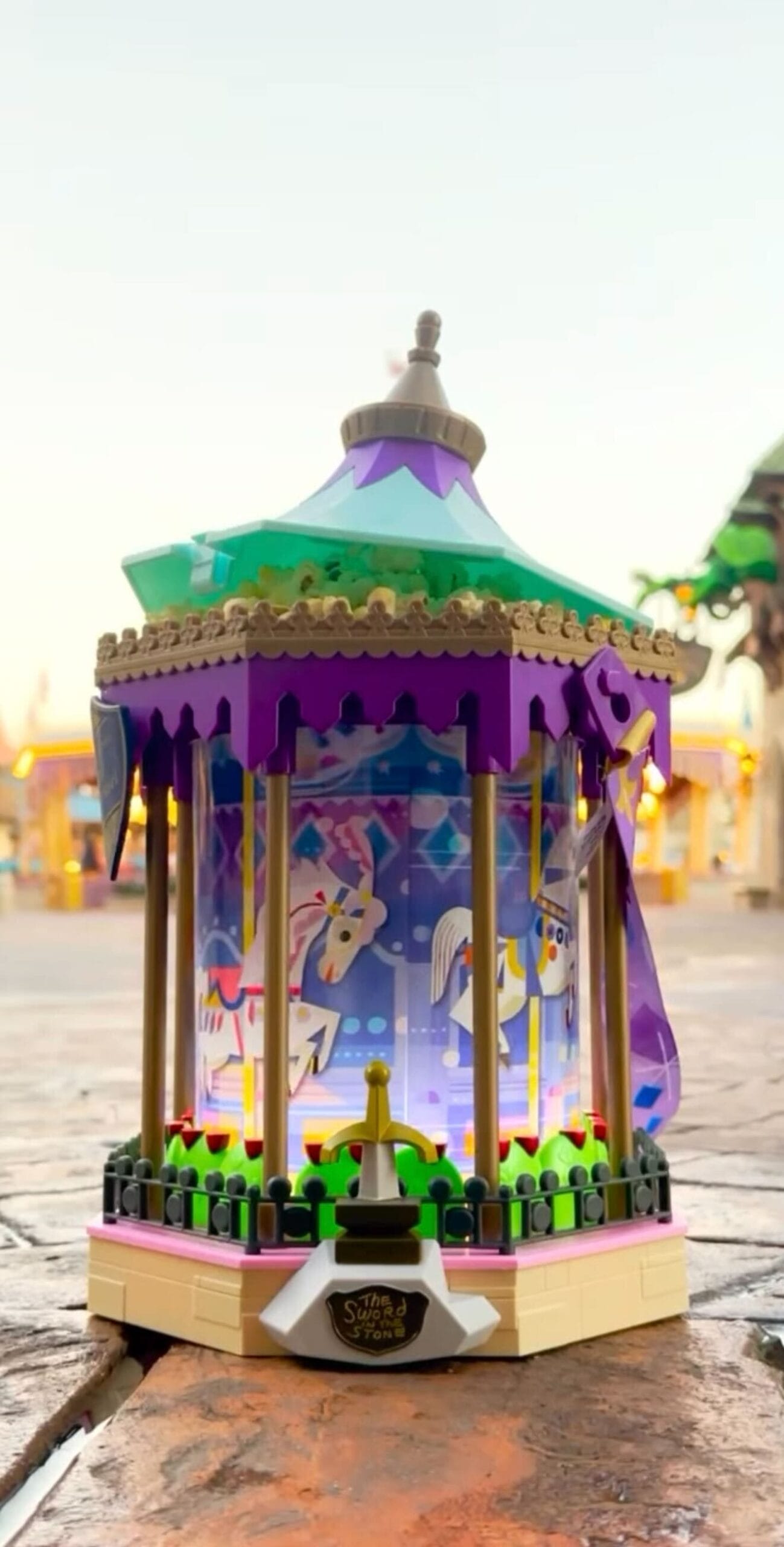 A small, colorful LEGO carousel with a hexagonal shape and with horse conditions that are decorated against a blurred background.