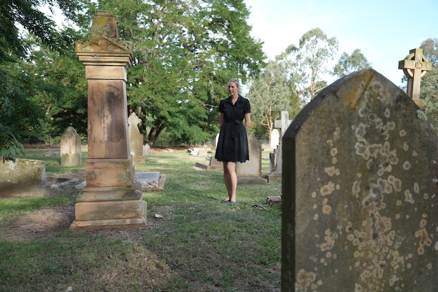 A woman in a black dress looks at damaged tombstones