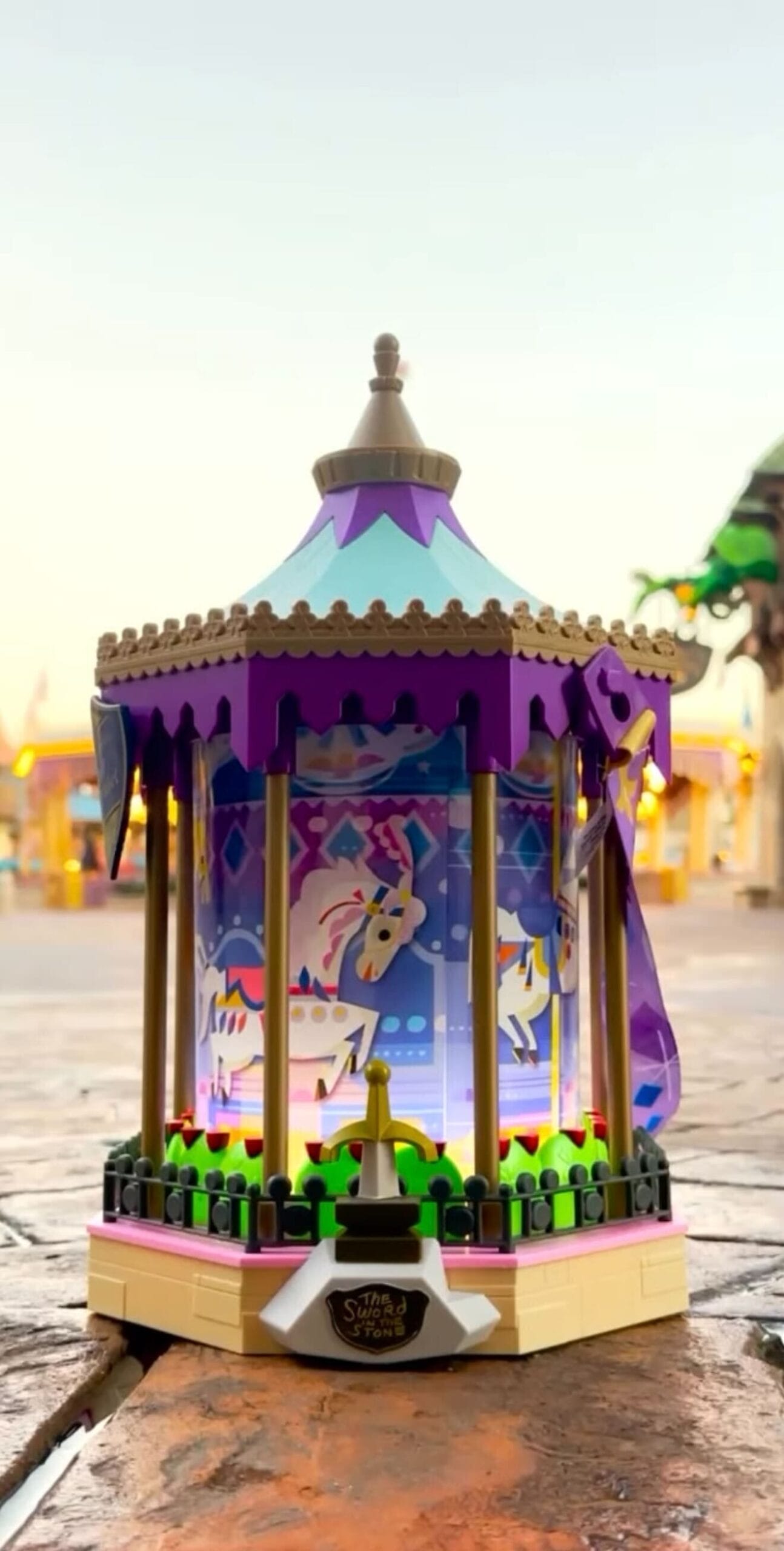 A decorative lantern with a carousel design has colorful horses and purple accents that rest on a stone surface under a clear sky.