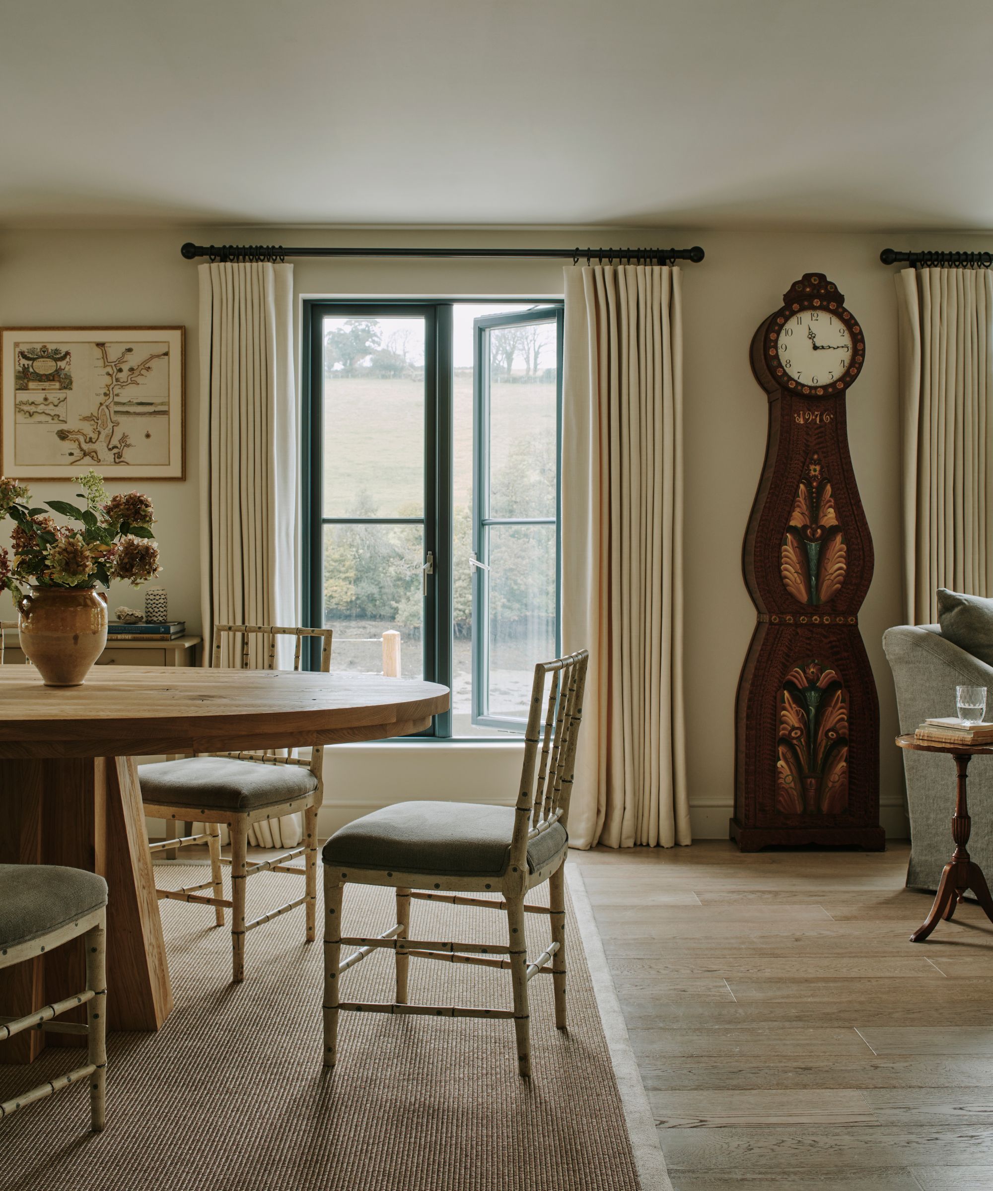 Neutral dining room with a large round wooden table and a large decorated mahogany -large clock