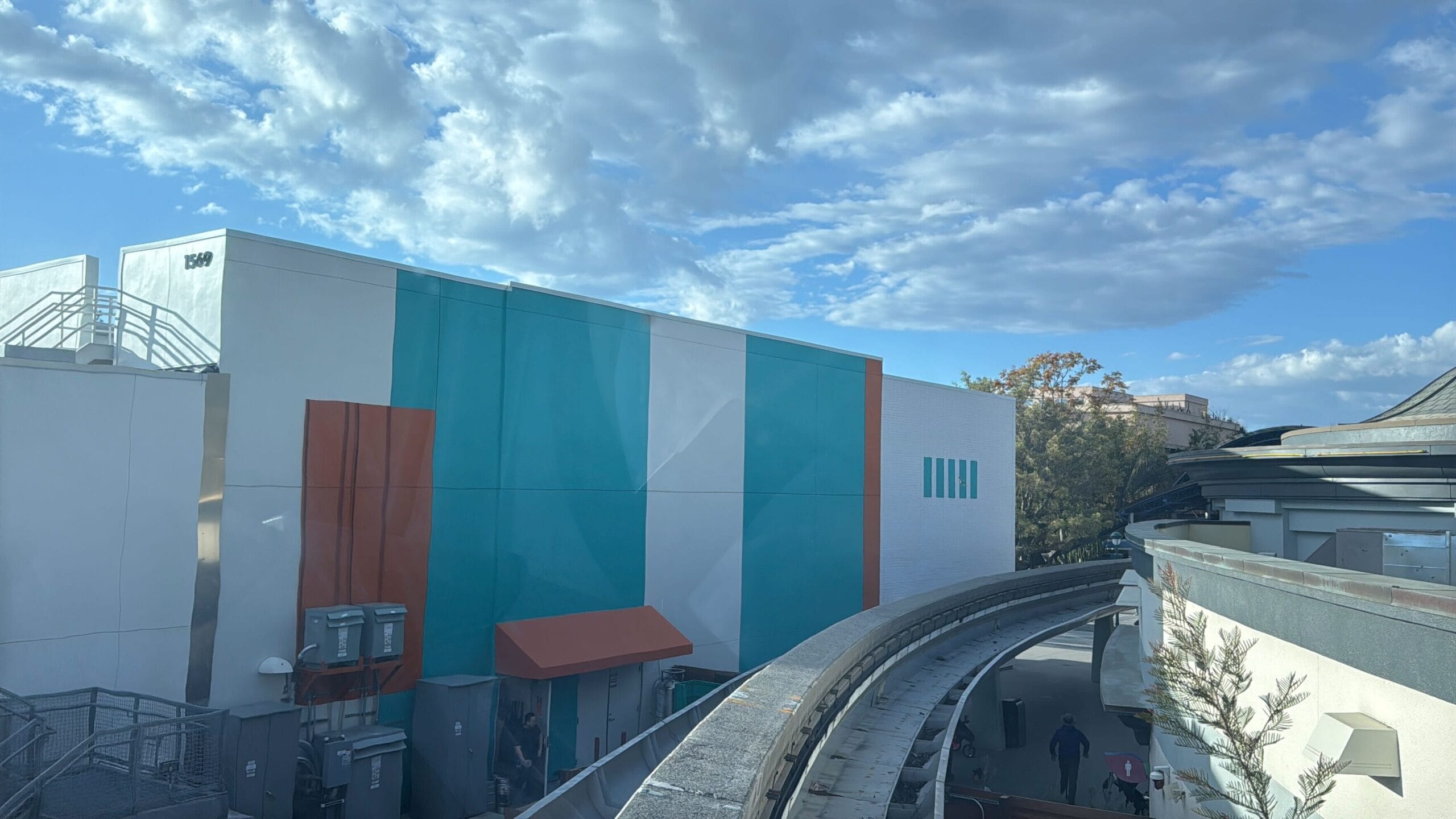 A building with blue -green, white and orange panels is under a cloudy sky, while the recently reopened Disneyland -Monorail stretch curves are graceful in the foreground.