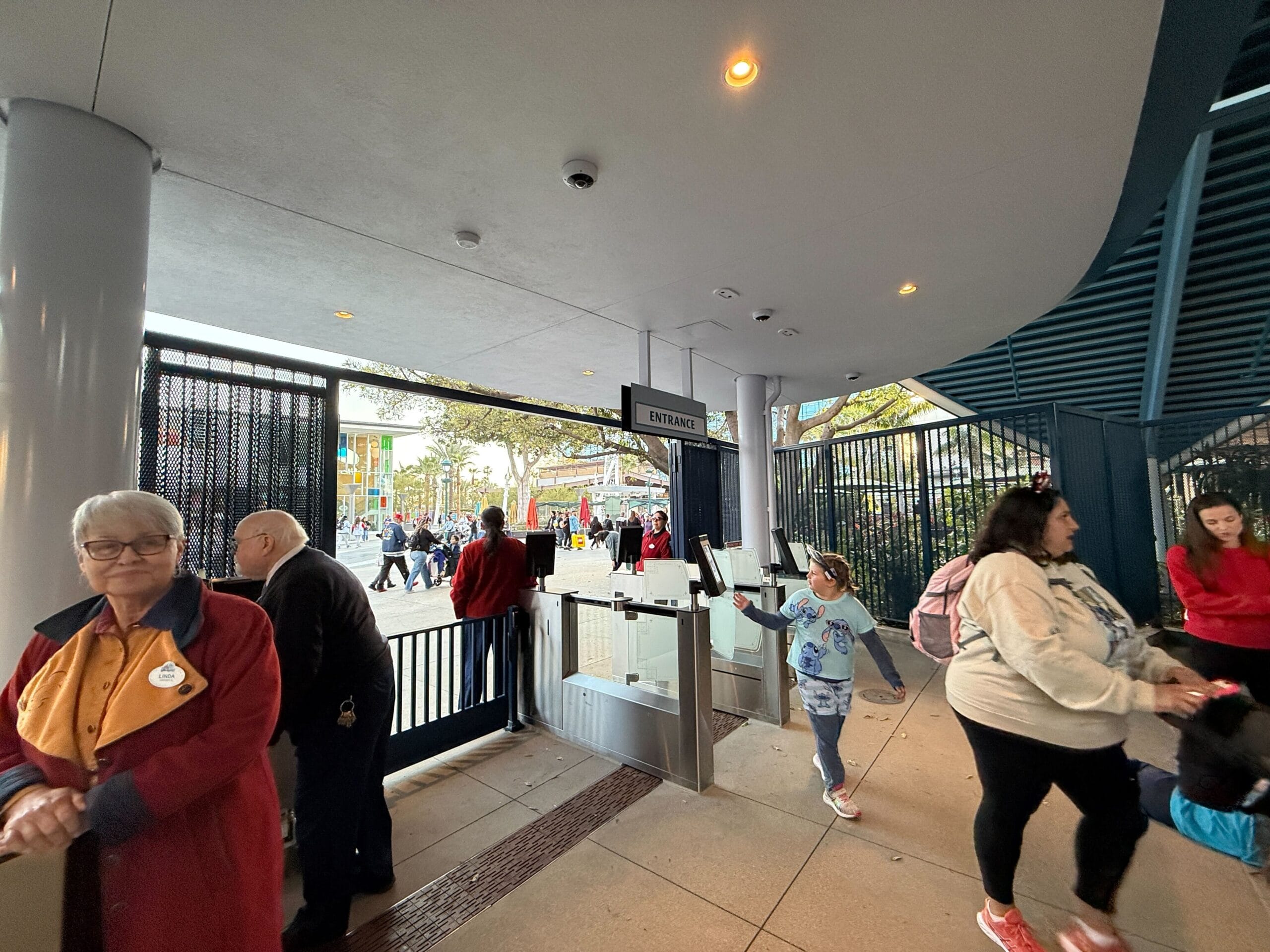 People who go through a security control point with metal detectors at the entrance to the Disneyland Monorail. A woman in a uniform is at the side and ensures that everything runs smoothly so that visitors want to go their magical journey.