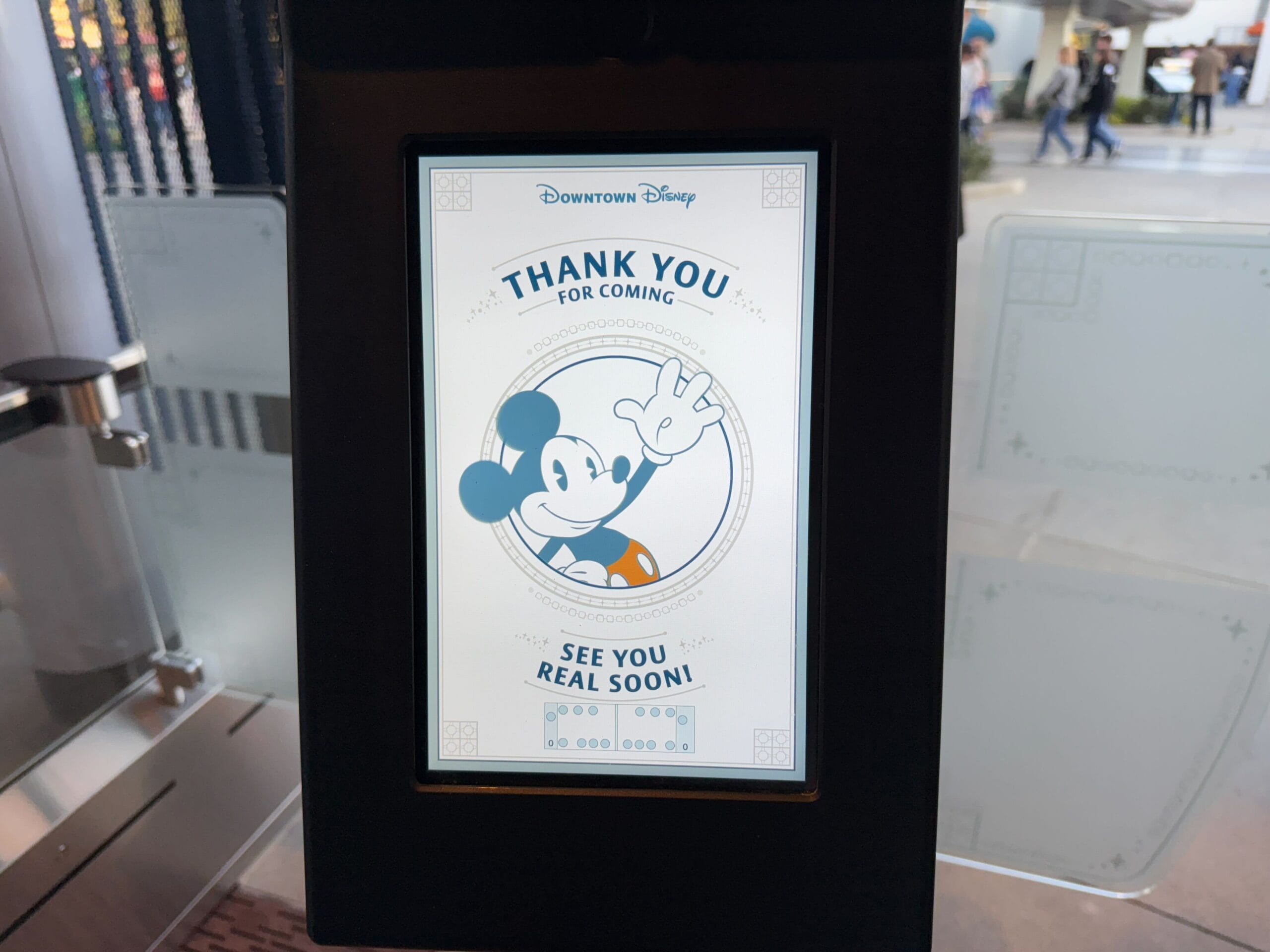 A screen in the city center of Disney shows a message with a cartoon character that waves and says "Thank you for coming" And "See you soon!" As Disneyland Monorail, glides smoothly in the background.