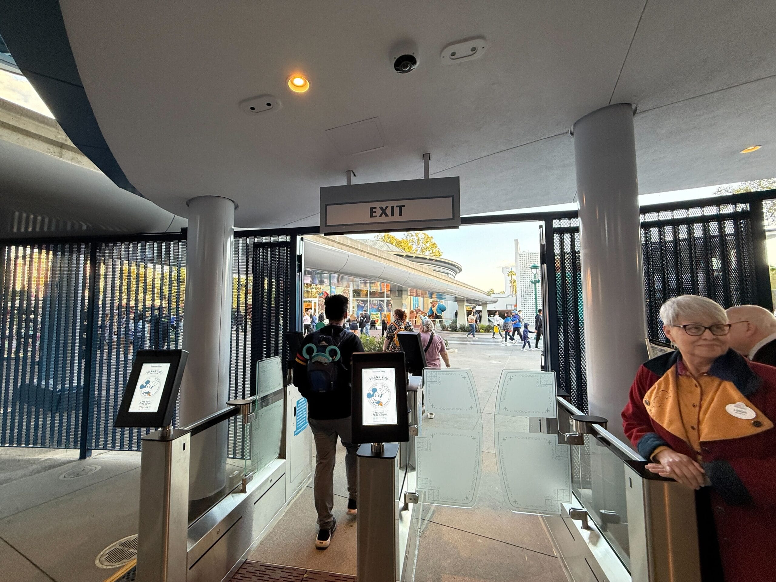 People who equip a building with an overhead from the exit through automatic goals look as if they could rise to Disneyland Monorail. On the right side is a person in a red and black jacket with a name tag.