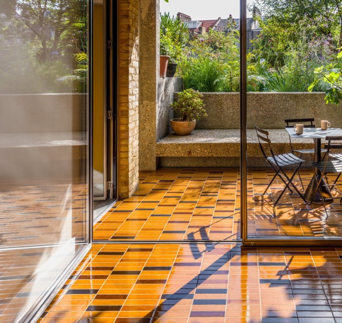 Earth tones decorate the floor inside a house and drive away on the terrace outside