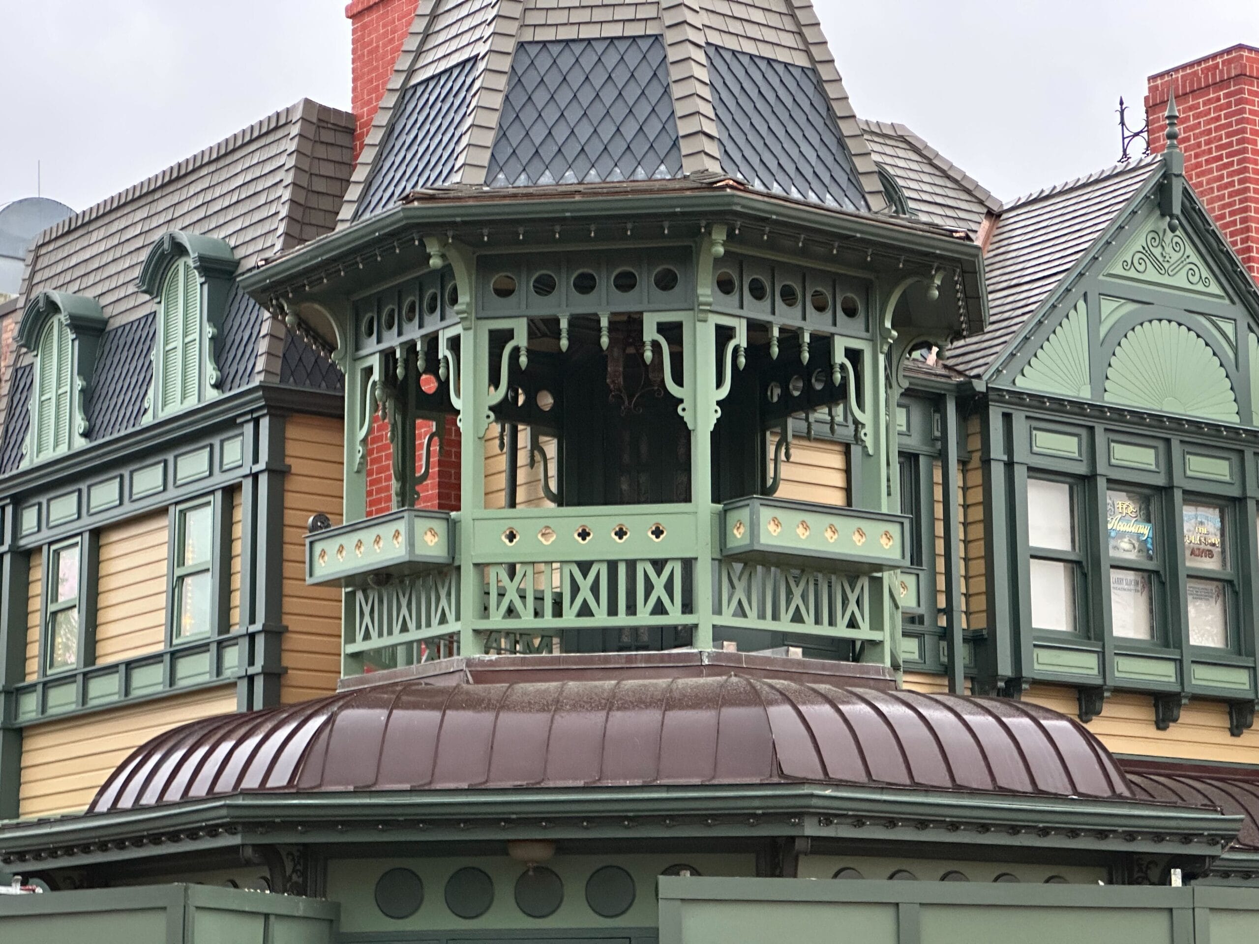 A Victorian style building with a detailed green wooden tower and decorative equipment. The exterior includes cream -colored siding, patterned shingles and brick accents.