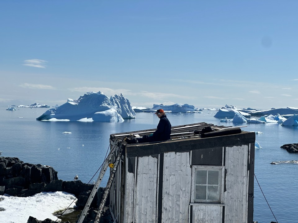 Person who sits on a weathered hut with a view of a glacier landscape.