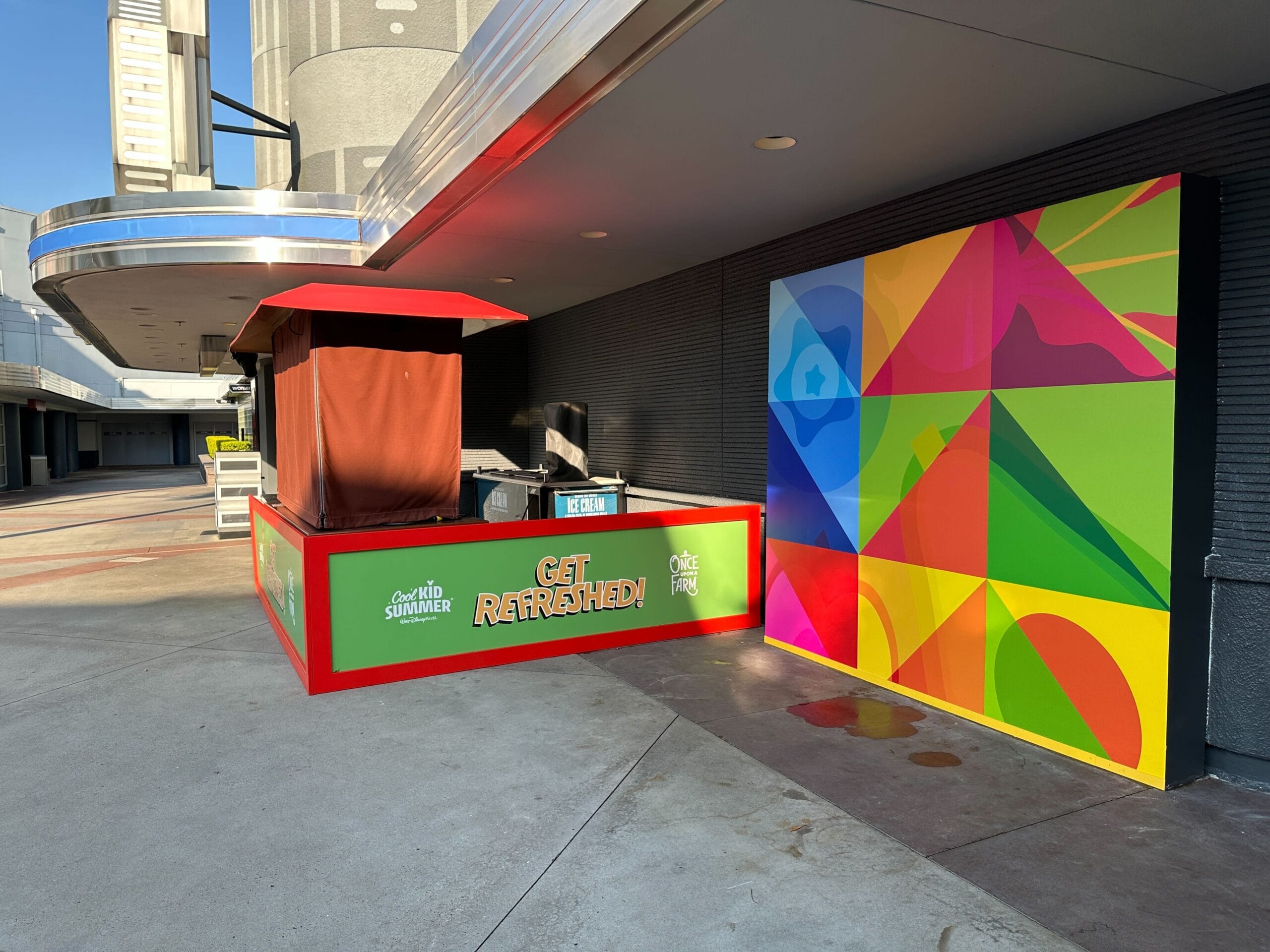 A closed refreshment stands in addition to a colorful geometric murals in a place outdoors.