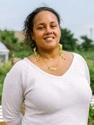 A woman with light brown skin and a white shirt that smiles into the camera.