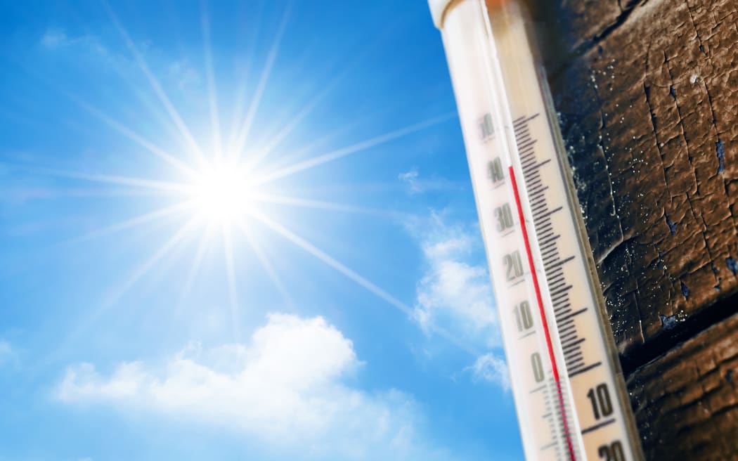 Thermometer with high temperature measurement on a scale against a background of bright sun and a blue sky with clouds. The concept of hot, dangerous weather, global warming