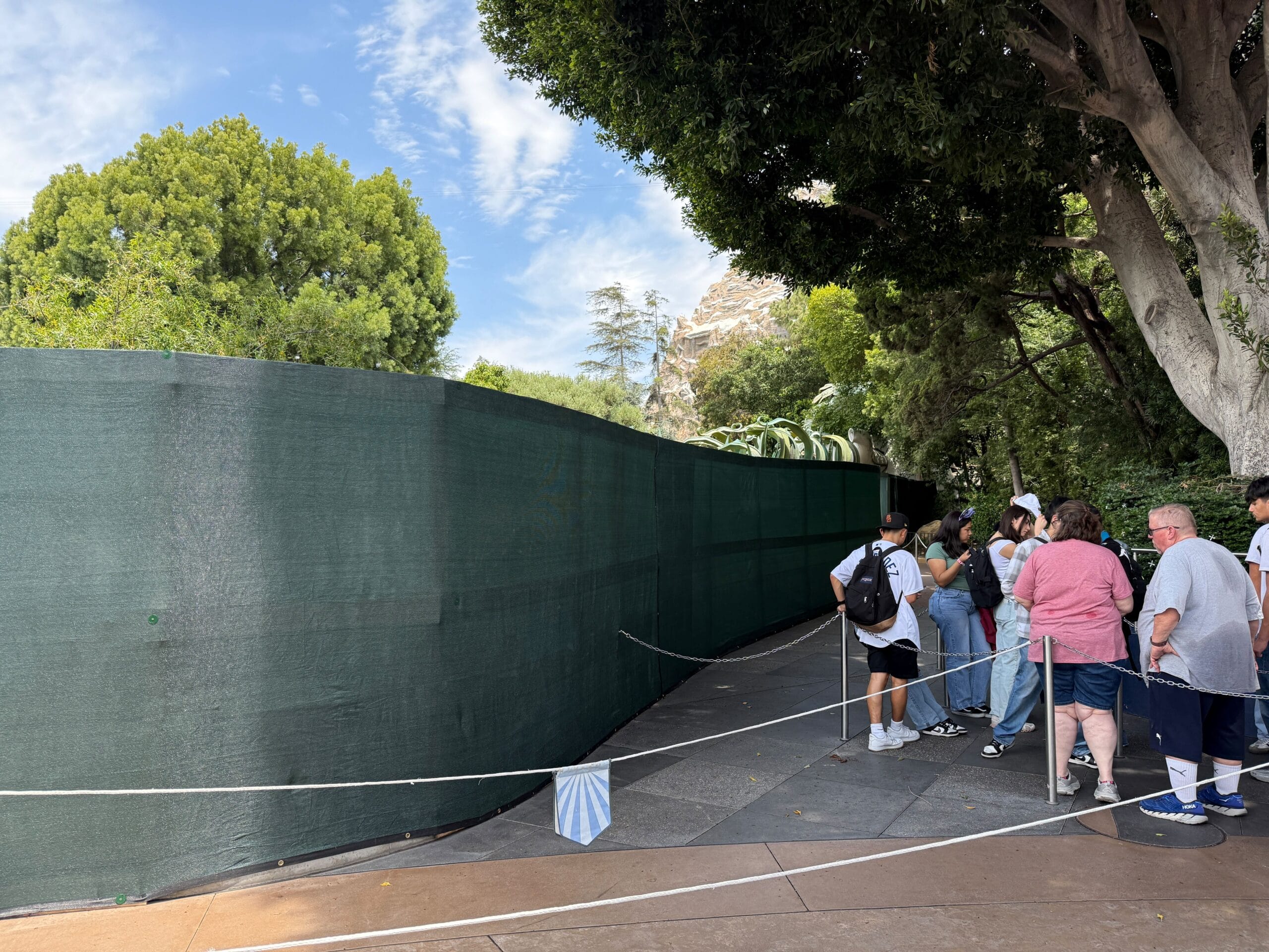 Several people are near a green construction block under trees on a sunny day, with the ropes mark from the area.