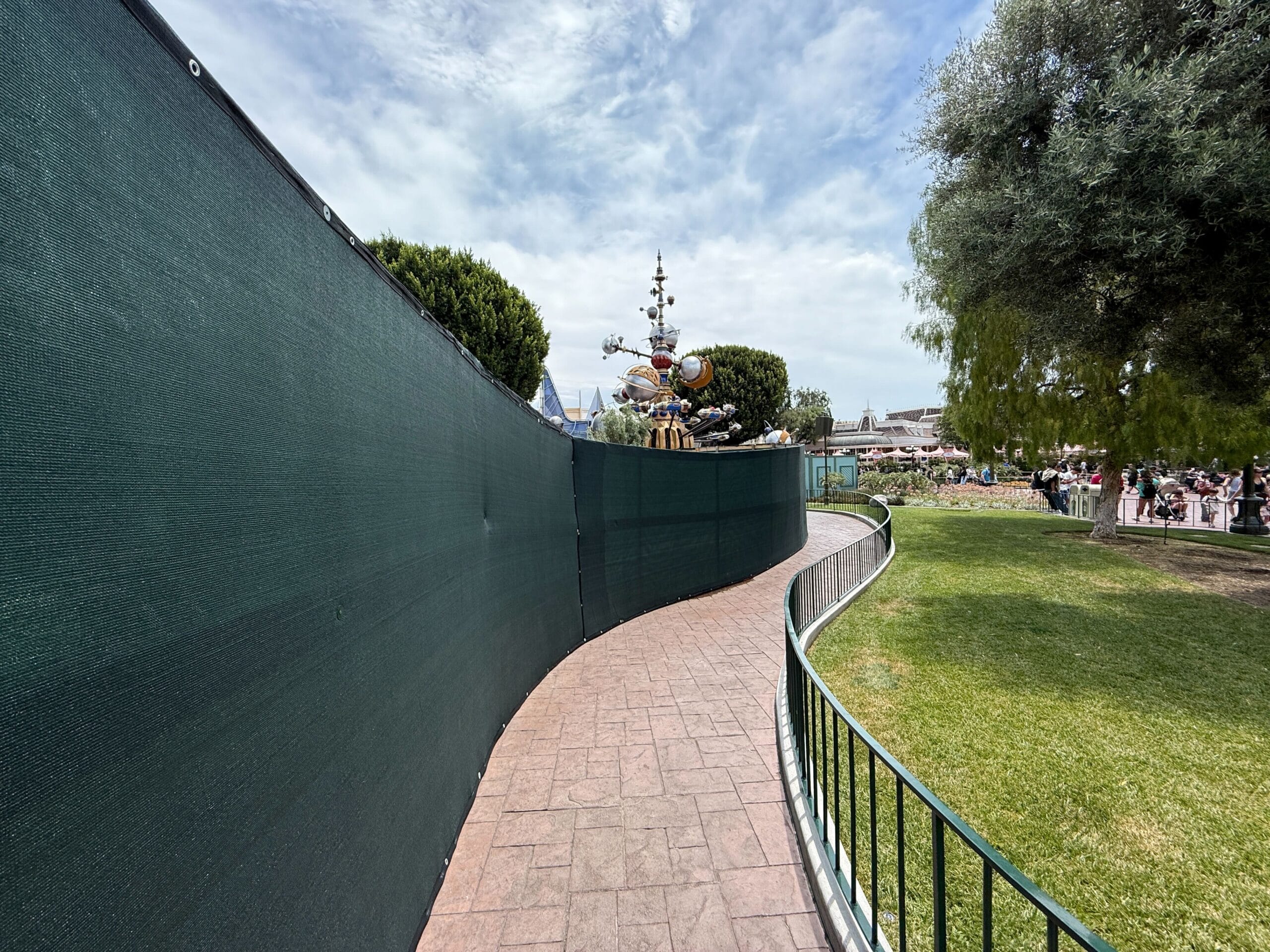 A curved sidewalk with green walls, grass and trees that leads to a thematic structure in the distance.