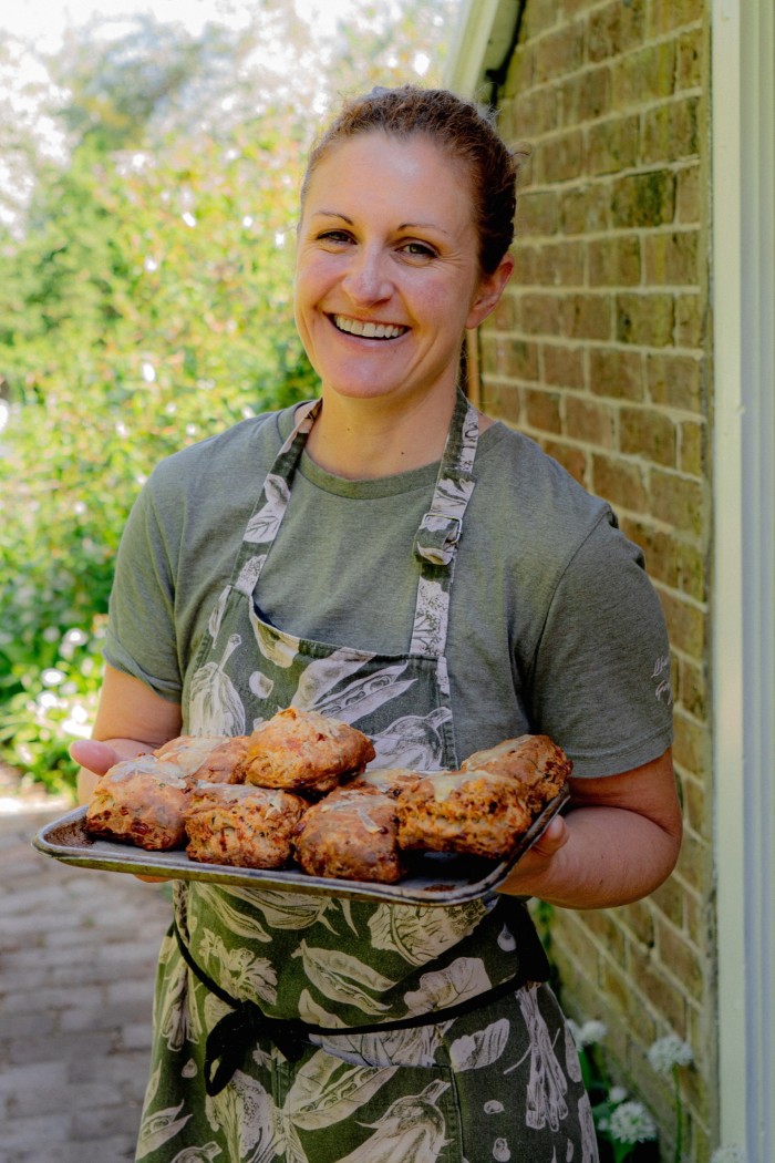 A woman who wears an apron holds a tray with scones.