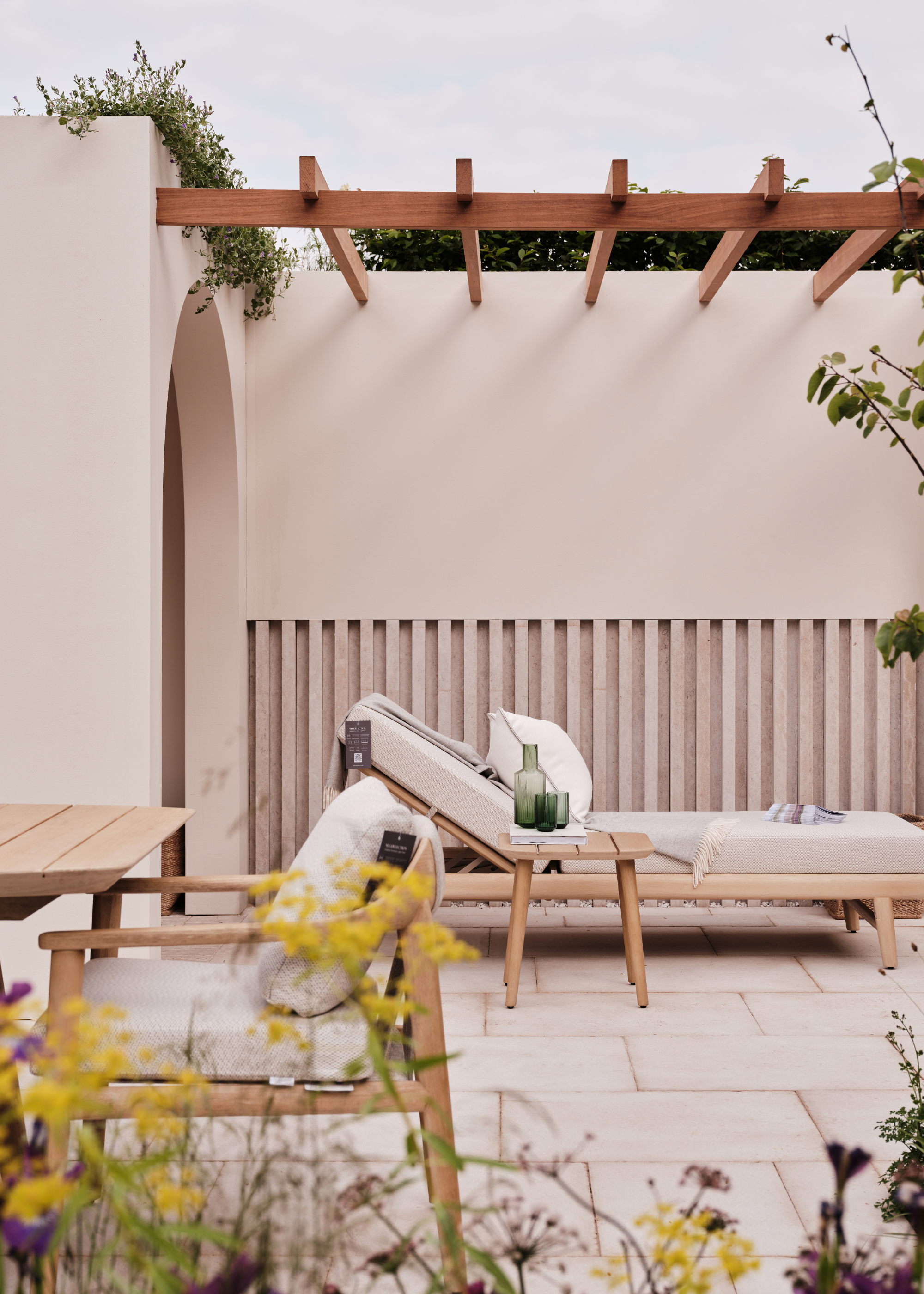 An exhibition of N -Ten degrees on the 2025 Chelsea Flower Show with a day bed outdoors and a side table with a glass carafe and a suitable green glasses