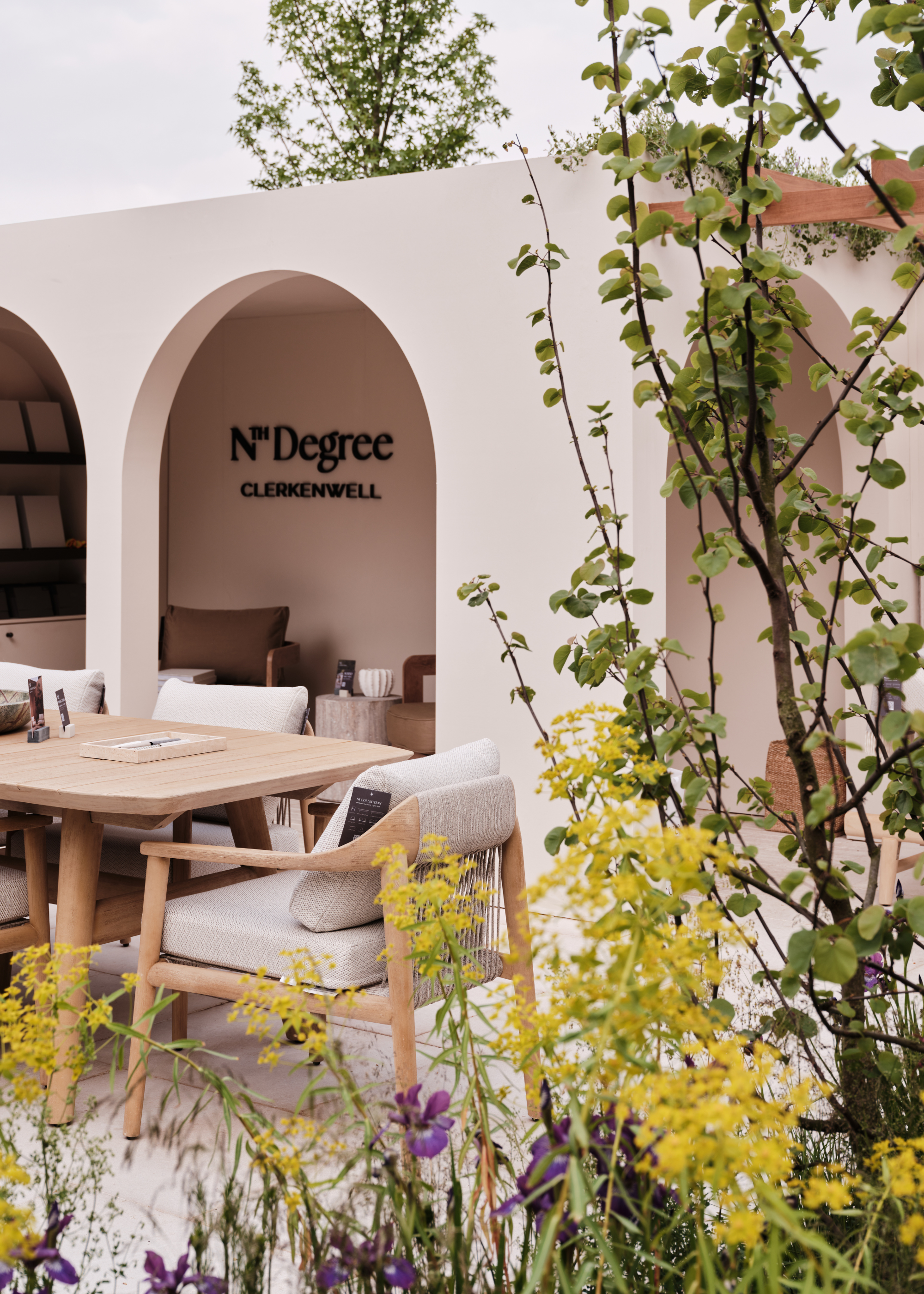 An exhibition of N -Ten degrees on the 2025 Chelsea Flower Show with an outdoor dining area next to a container garden made of colorful flowers and green leaves