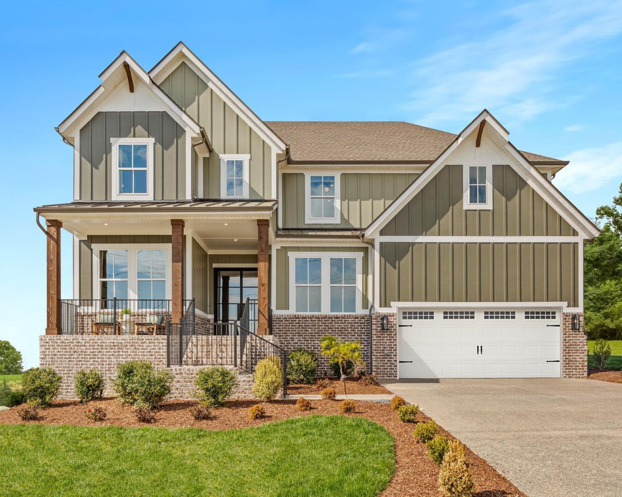 The exterior of a large house in a steamed sage green with a white garage, a driveway and a dependent front garden.