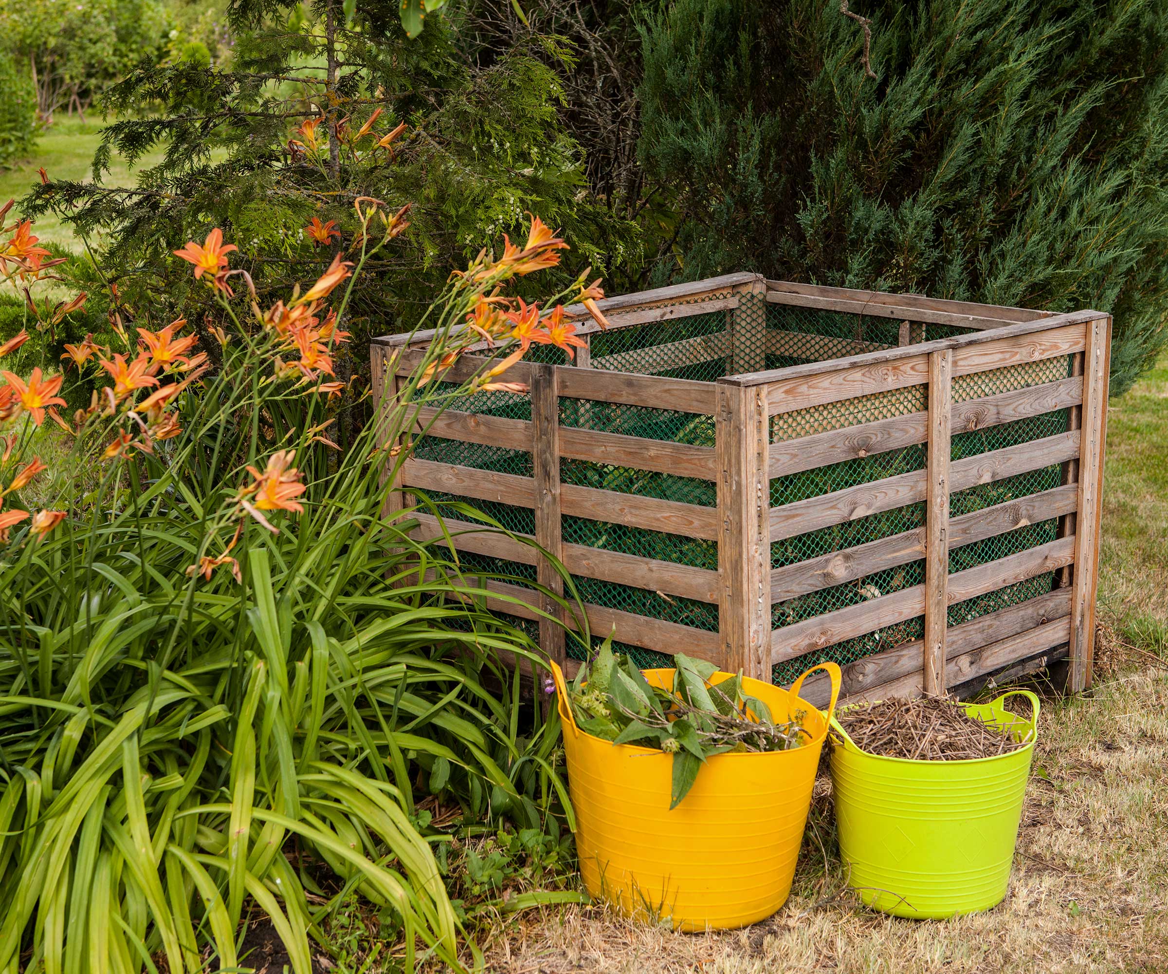 Compost container in a garden with colorful buckets