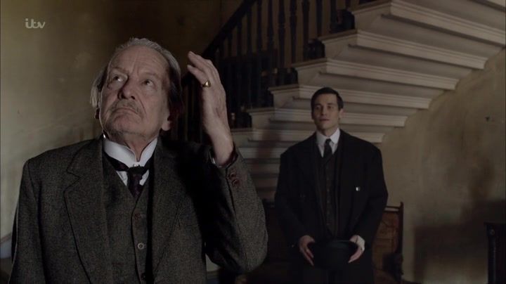 Scene from downtown Abbey: An older man wears in a tweed suit while a younger man is behind him in a dark suit.