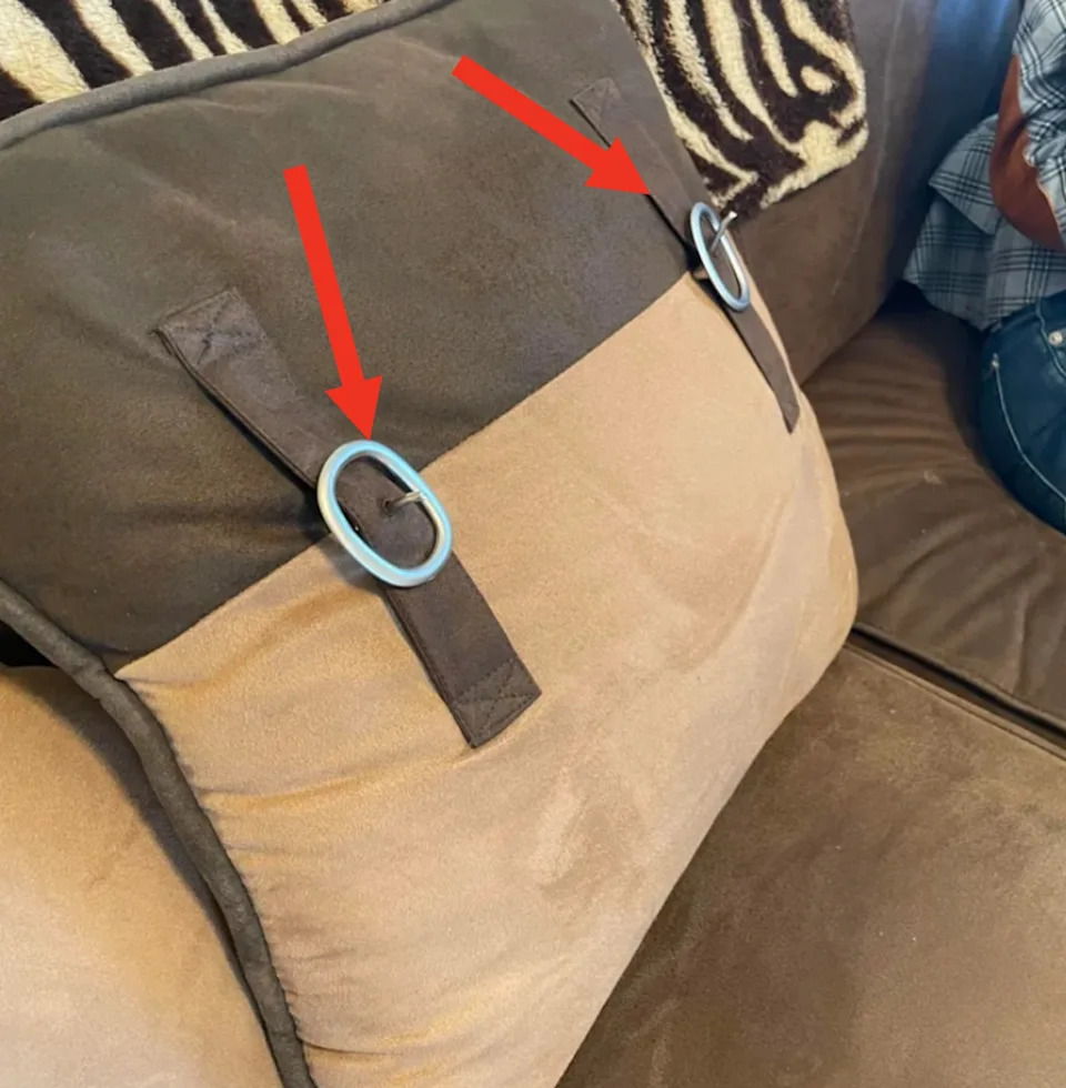 One person teaches himself on a couch that holds a baby next to a decorative pillow with button details
