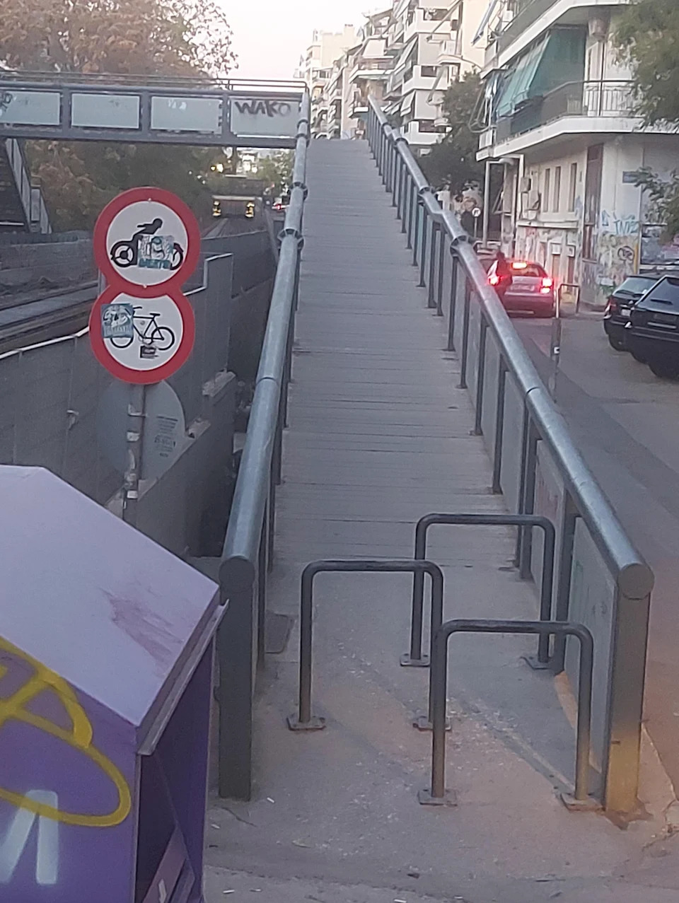 Pedestrian overpass with bicycle and motorcycle ban sign; Cars visible on the street nearby