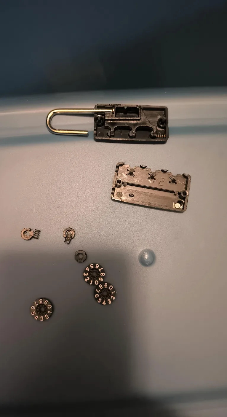 Open combination lock broken down into parts, including dial numbers and inner mechanics, placed on a flat surface