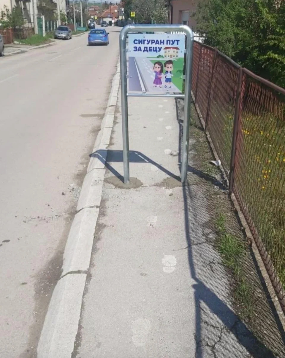 A street sign shows a cartoon of children that cross a street with text that is translated "Safe way for children" in Serbian