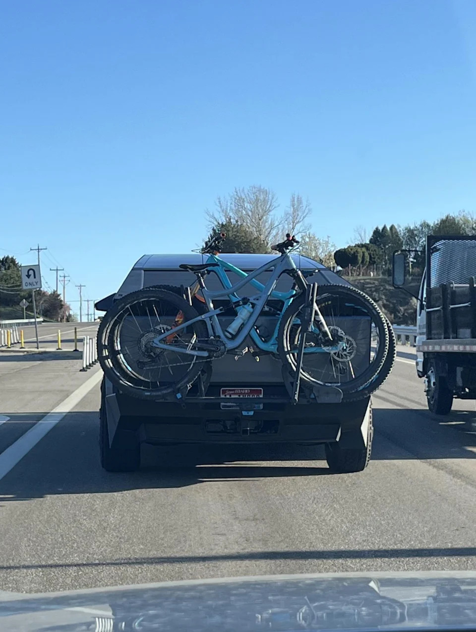 The vehicle on the highway has installed bicycles on the rear bicycle shelf. Street and trees visible in the background