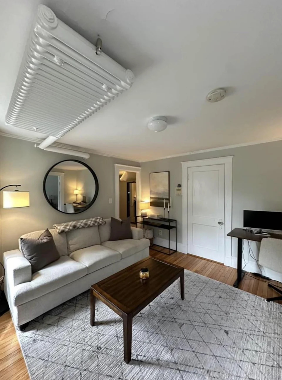 Modern living room with a sofa, round mirror, wall art and television. A coffee table on a patterned carpet completes the decor