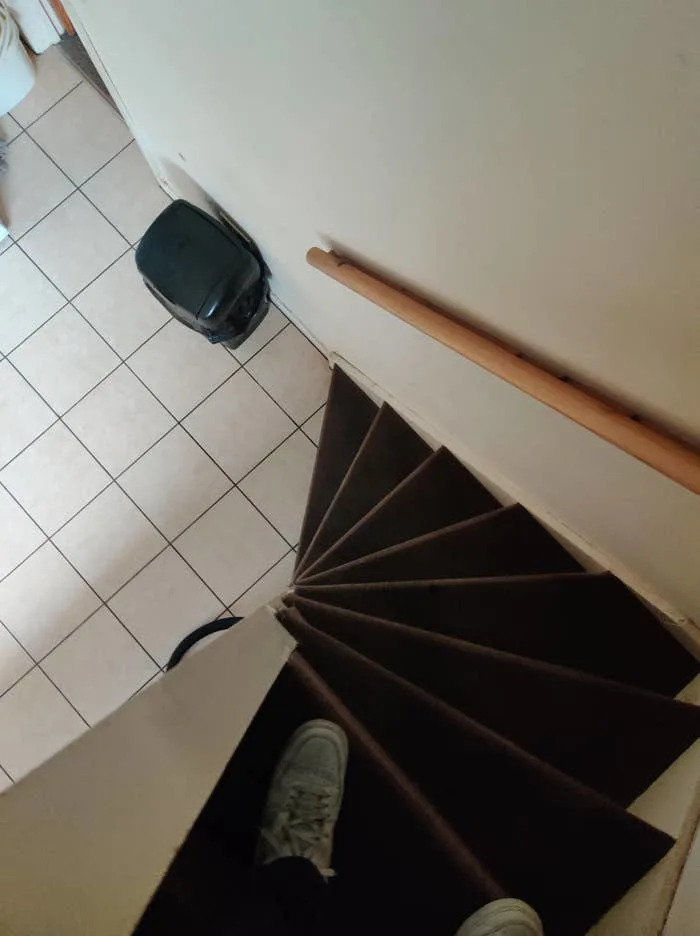 Steeper, narrow spiral staircase with wooden railing, designated from above. The feet of a person in sneakers are visible on the top of the staircase