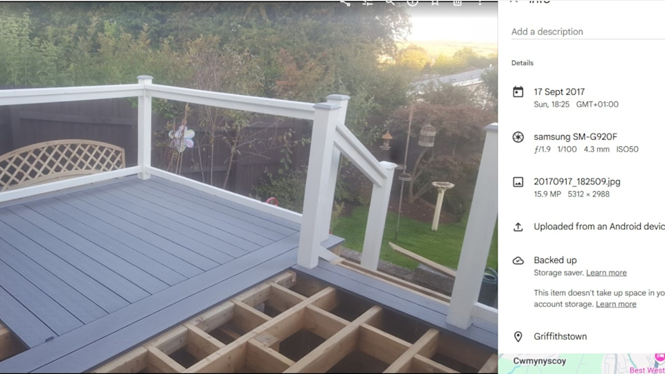 Gray deck with white fences is levied from a small garden. At the top of the picture, an increased wooden platform can be seen on which the deck bottom is unfinished. The location and the time stamp of the picture are dated on the right side until September 17, 2017.