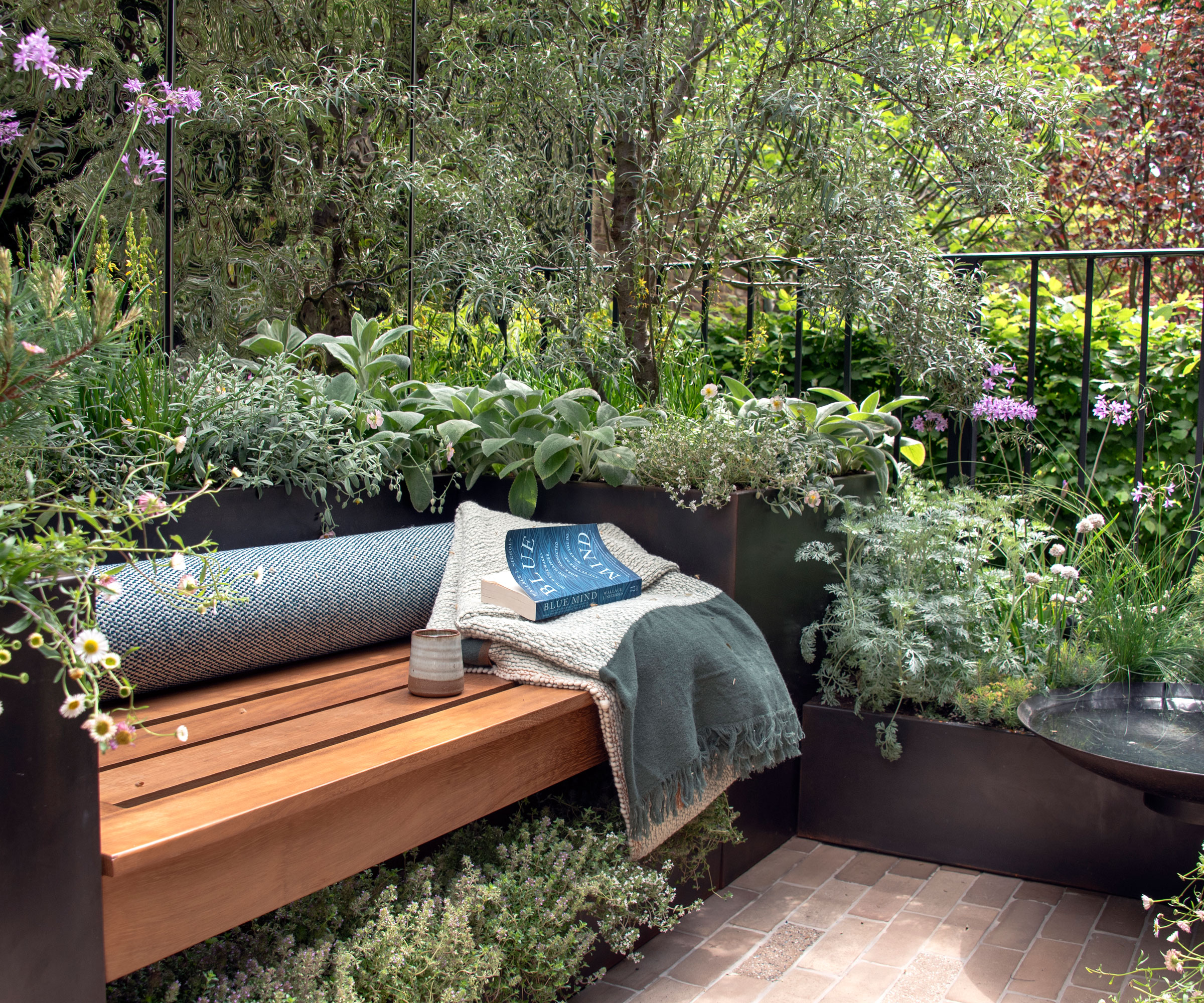 Small balcony garden with bench, throw, coffee cup, book and plants