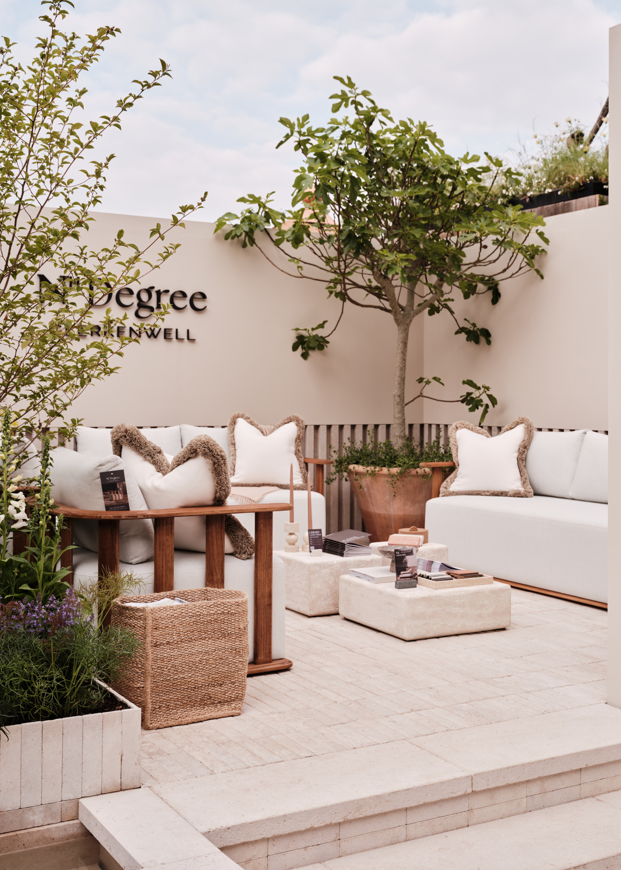 An exhibition of n-ten degrees on the 2025 Chelsea Flower Show with outdoor sofas, block coffee, a woven basket, a shrub in a trog style container and a pot tree