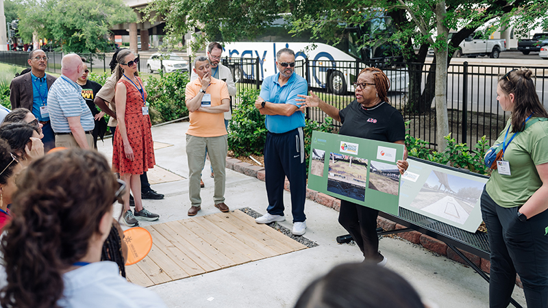 A woman holds a poster board and speaks to a group of people in a rainwater management park. 