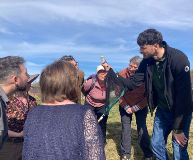The group of people gathered in a circle, with a man holding up a sample collection pipe. Everyone looks at the tube and smiles.