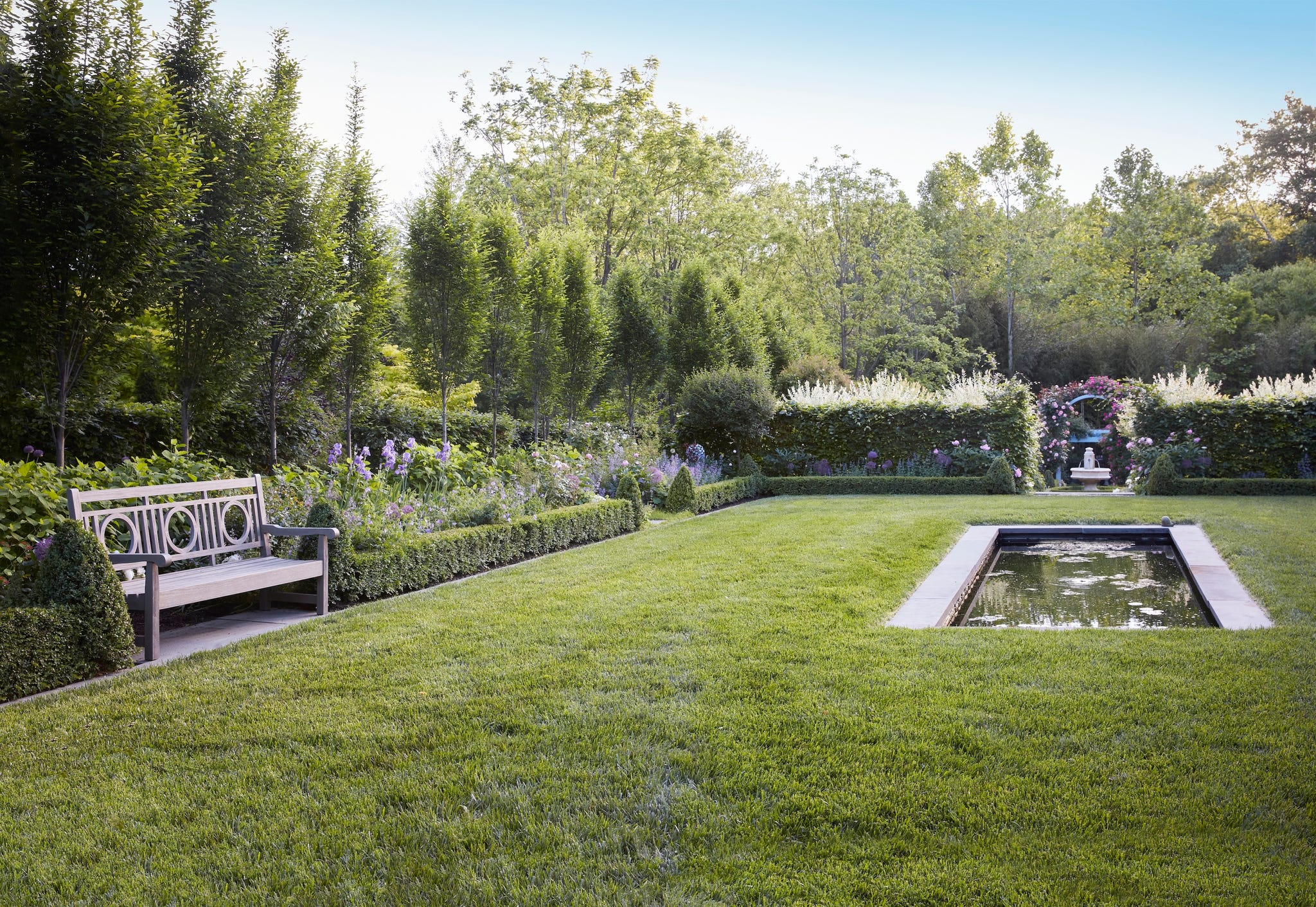 Garden in the north virginia home of the gardener Yvonne Tsikata. A teak bank (Restoration Hardware), which is embedded between the boxing wood hedges, is an inviting perch for a break next to a reflective pool that is inspired by the 16th century Wollerton Old Hall Garden.