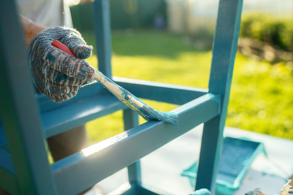 Senior Man renovates an outdoor chair in the back yard on the sunny evening. Old furniture renovation. Sustainability concept.
