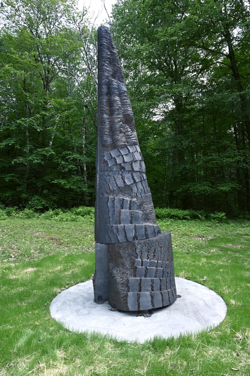 A conical, black, abstract sculpture of Yō Akiyama installed outdoors